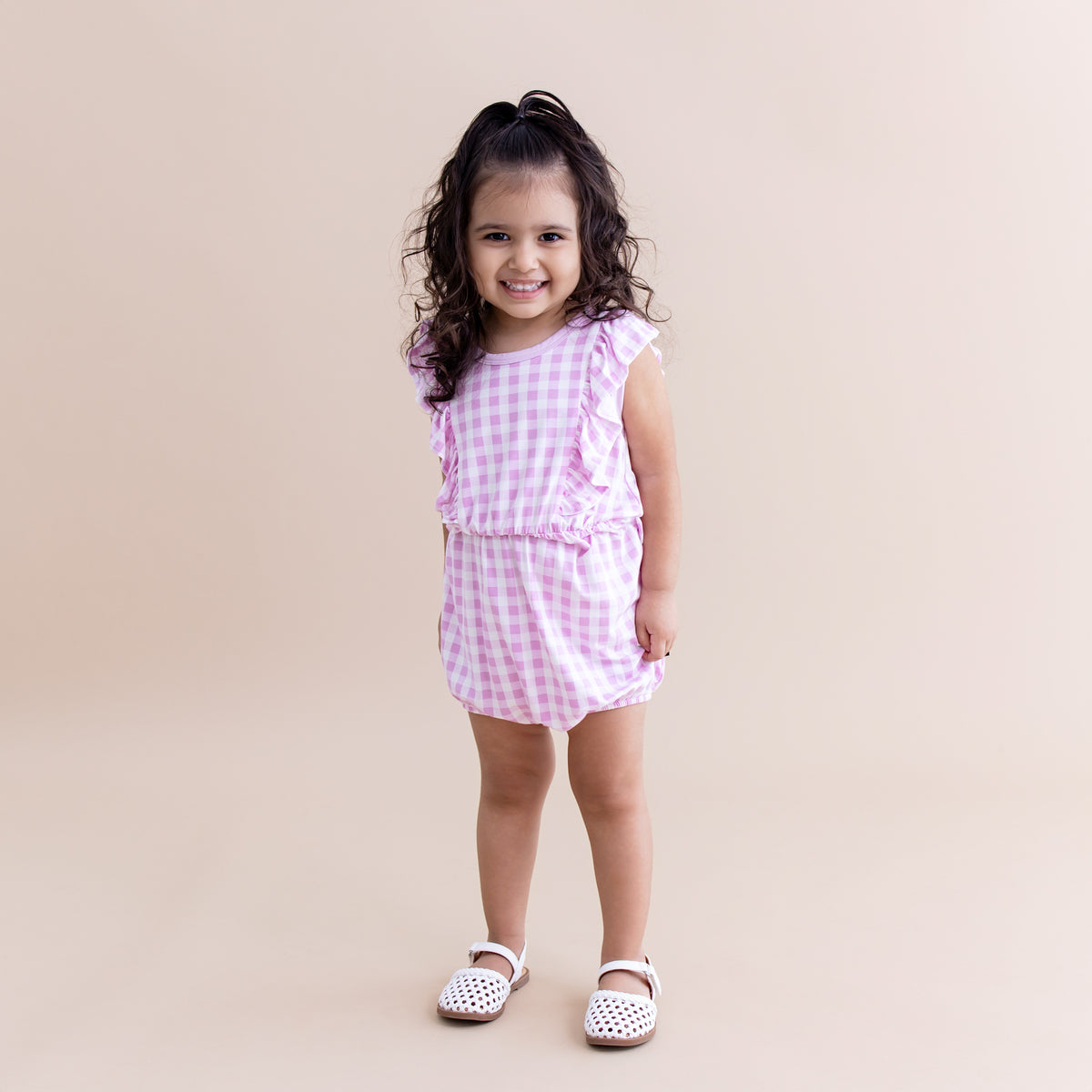 Young girl wearing the Bubble Romper in Gingham Thistle with white sandals