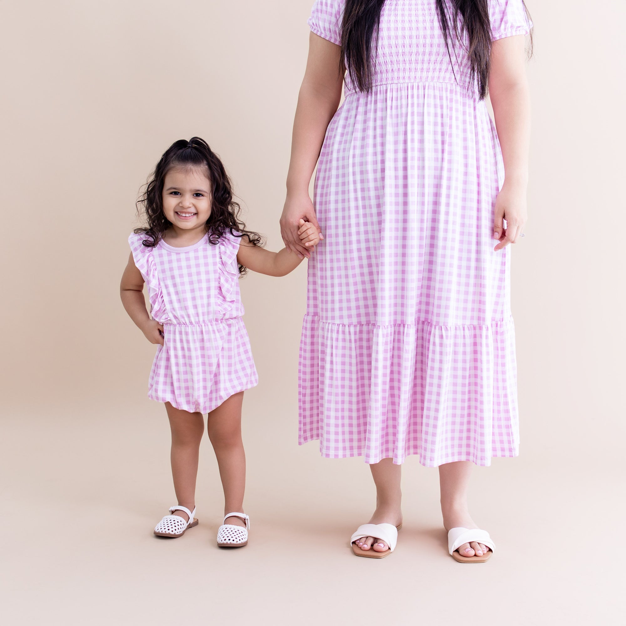 Young girl wearing the Bubble Romper in Gingham Thistle holding her mothers hand who is matching in a women's smocked dress