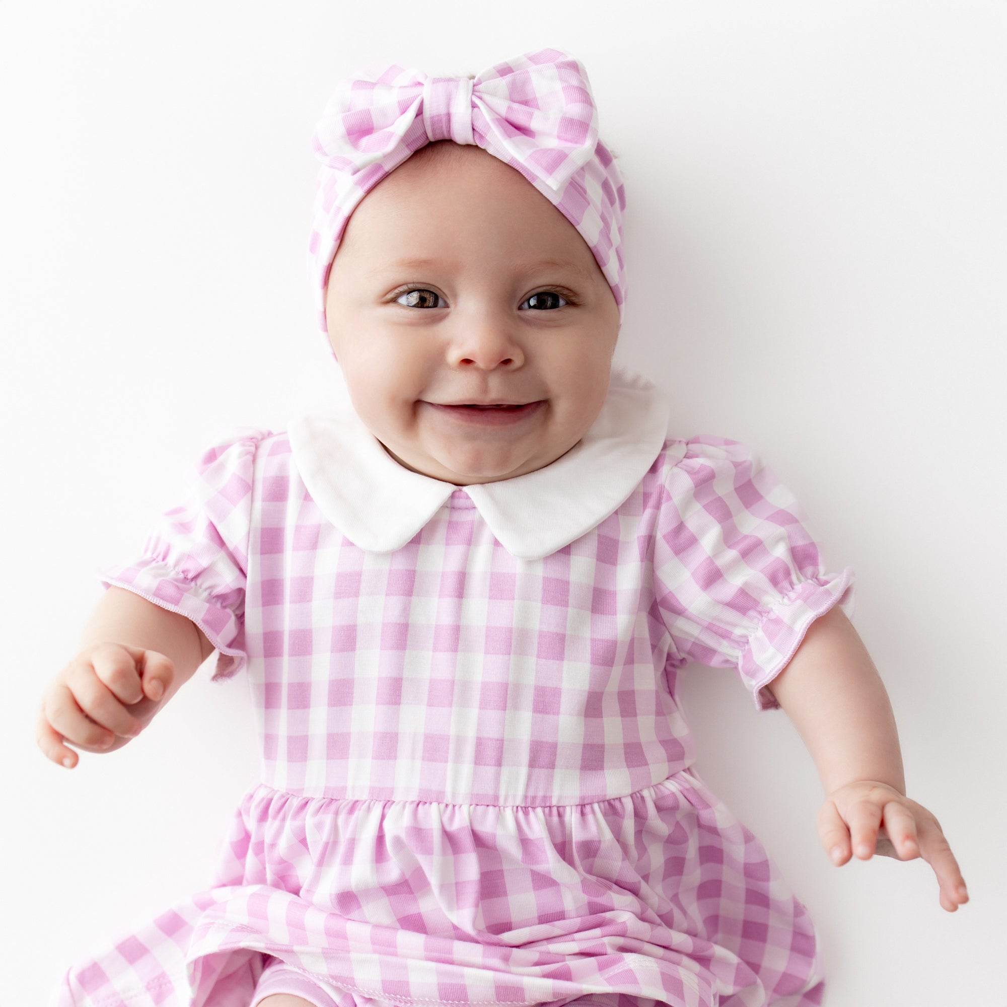 Close up of smiling infant wearing the Peter Pan Collar Bodysuit Dress in Gingham Thistle