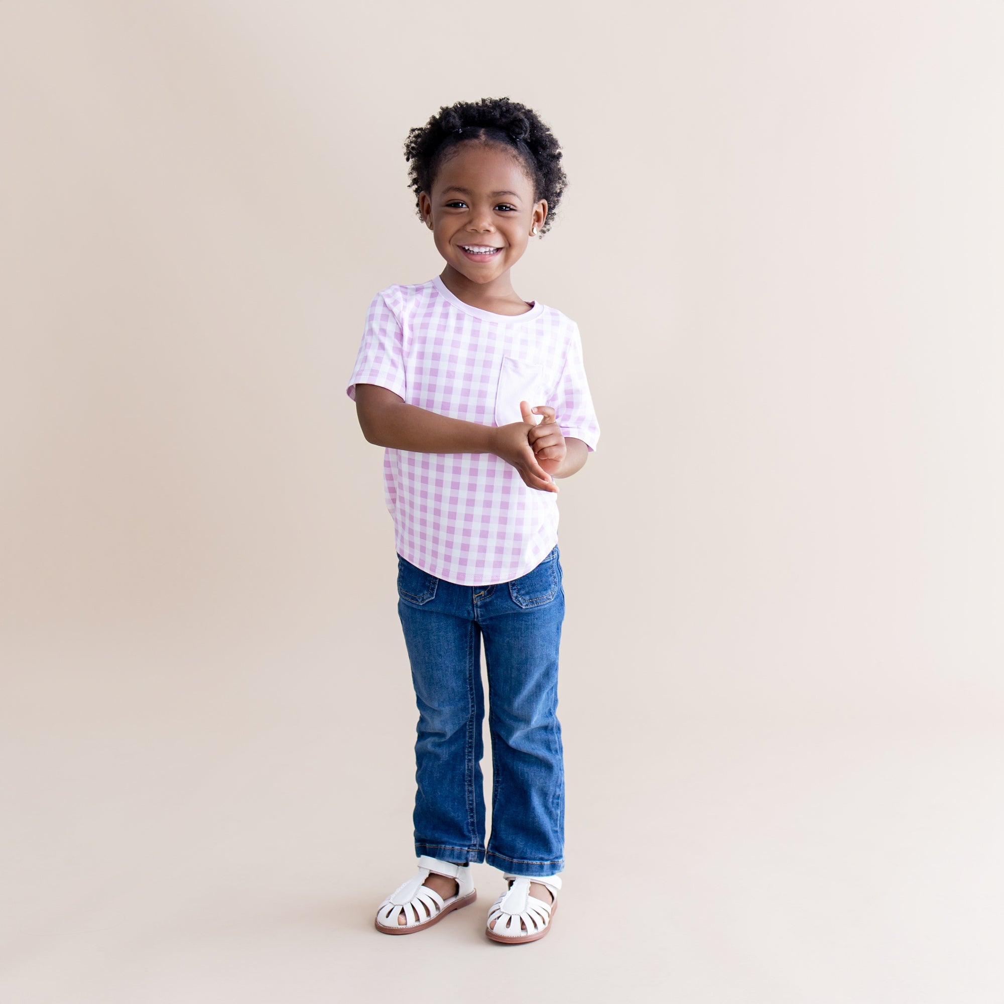 Young girl posing wearing the Toddler Crew Neck Tee in Gingham Thistle with dark denim jeans and white sandals