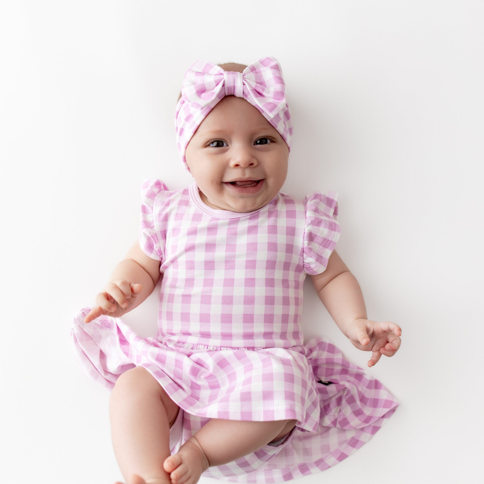 Close up of infant wearing the Twirl Bodysuit Dress in Gingham Thistle with matching bow headband