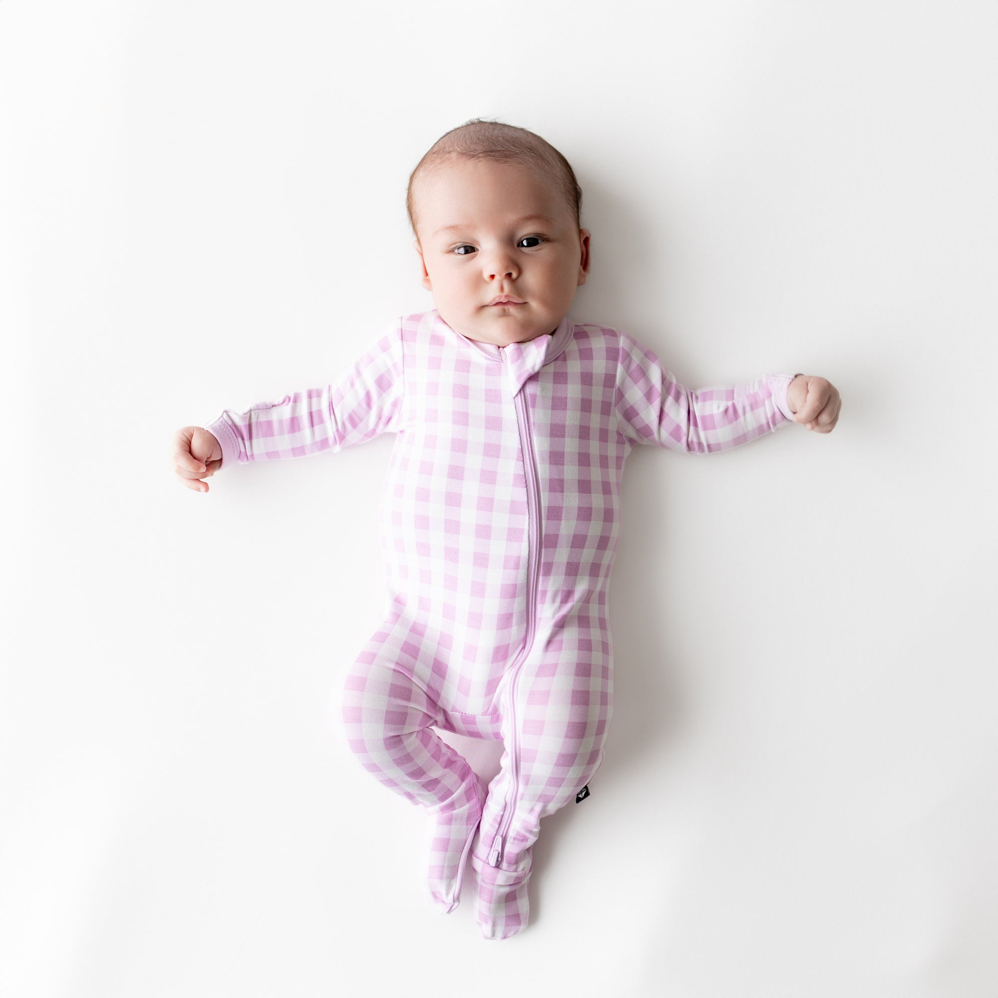 Infant wearing the Zippered Footie in Gingham Thistle laying on a white surface