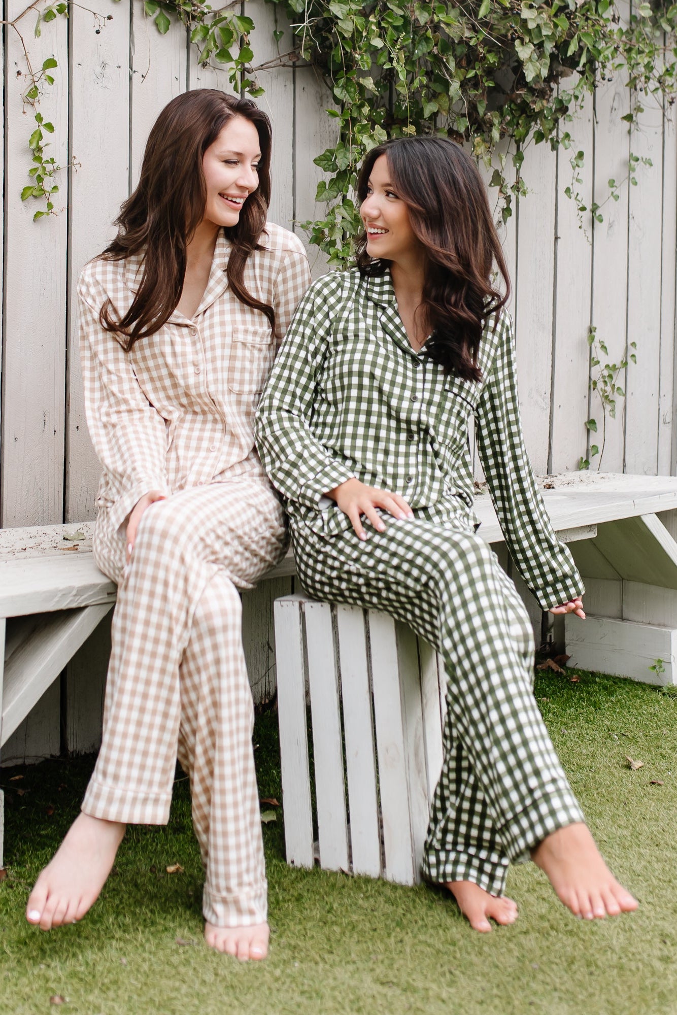 Two female models sitting on a white bench wearing the Long-Sleeved Women's Pajama Set in Gingham Bisque and Gingham Fir