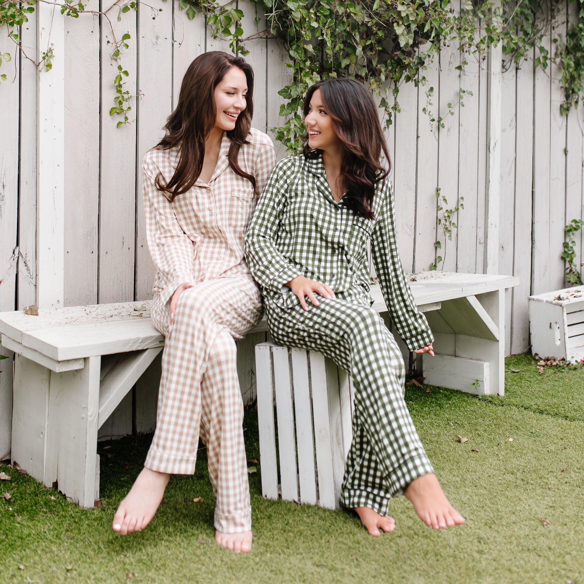 Two female models sitting on a white bench wearing the Long-Sleeved Women's Pajama Set in Gingham Bisque and Gingham Fir