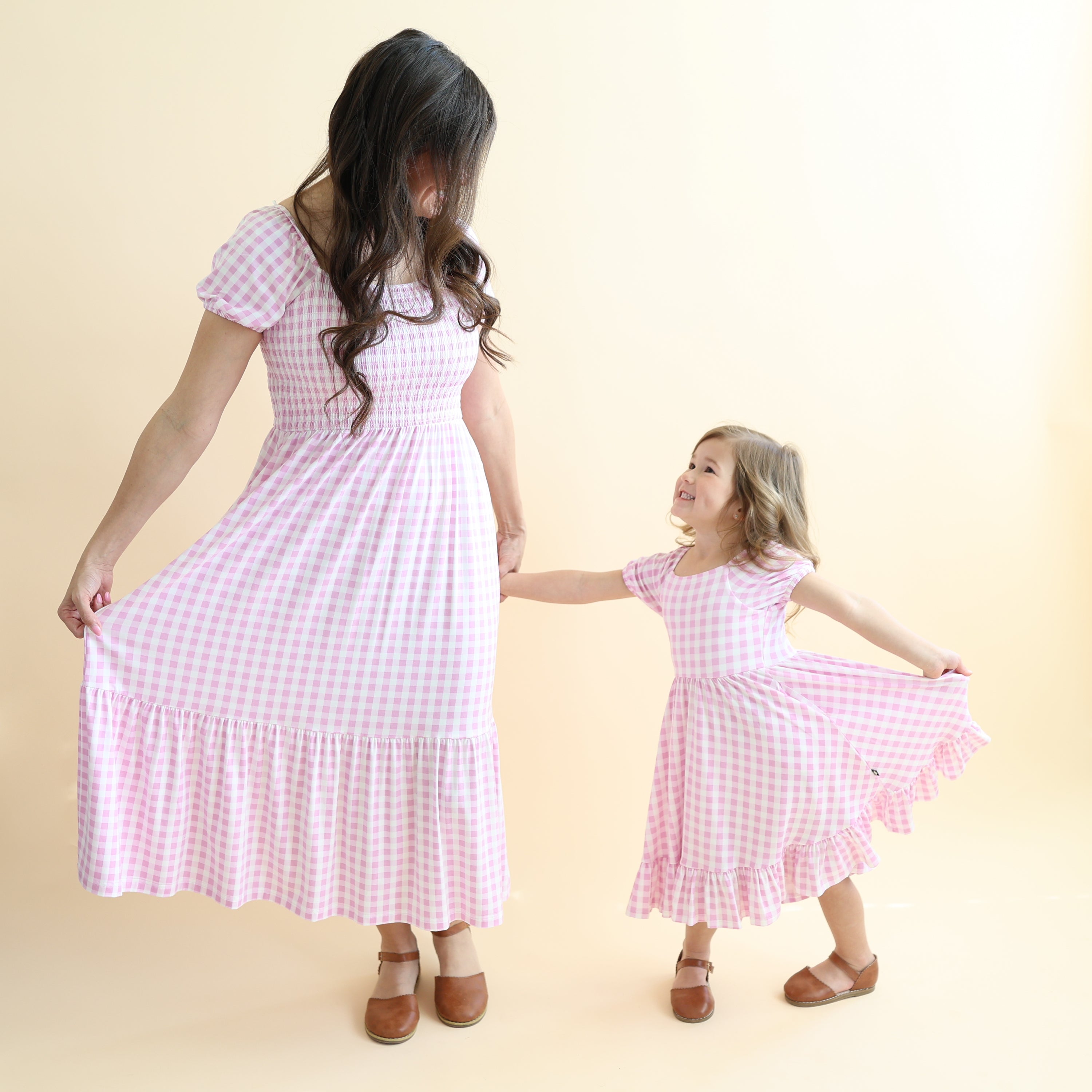 Mother and daughter holding hands looking at one another matching in Smocked dresses in Gingham Thistle