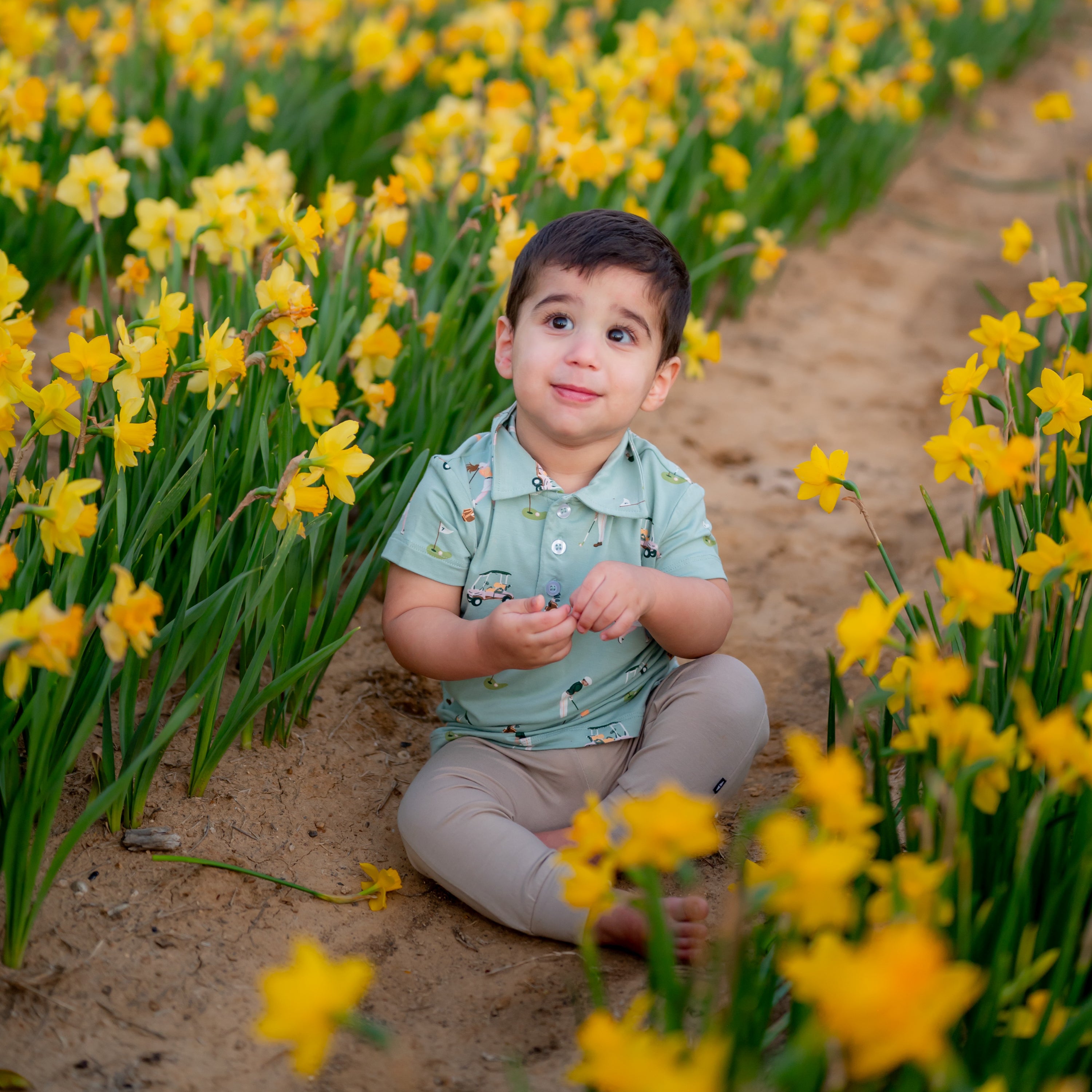 Toddler smiling surrounded by yellow flowers wearing Golf Polo