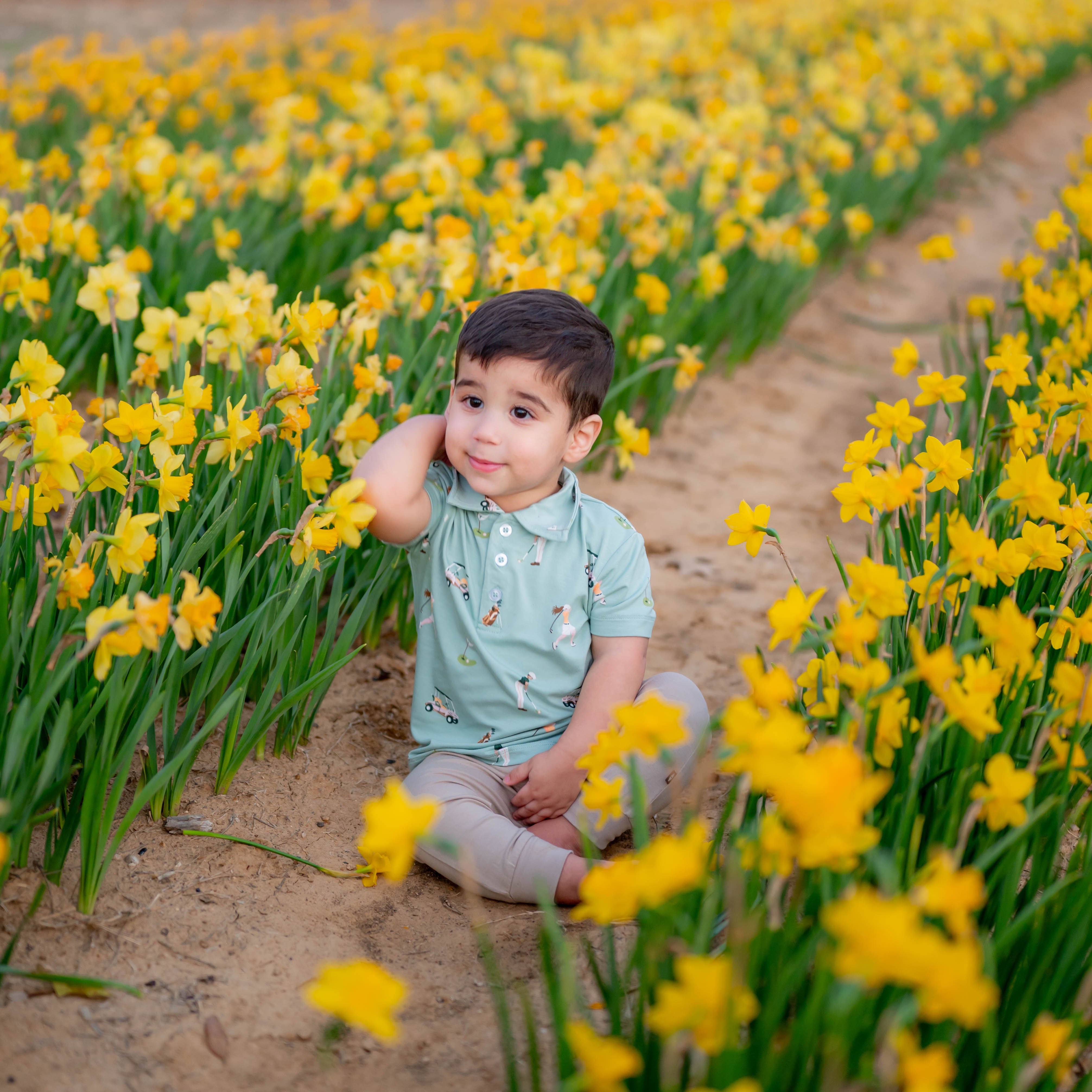 Toddler sitting surrounded by yellow flowers wearing Golf Polo