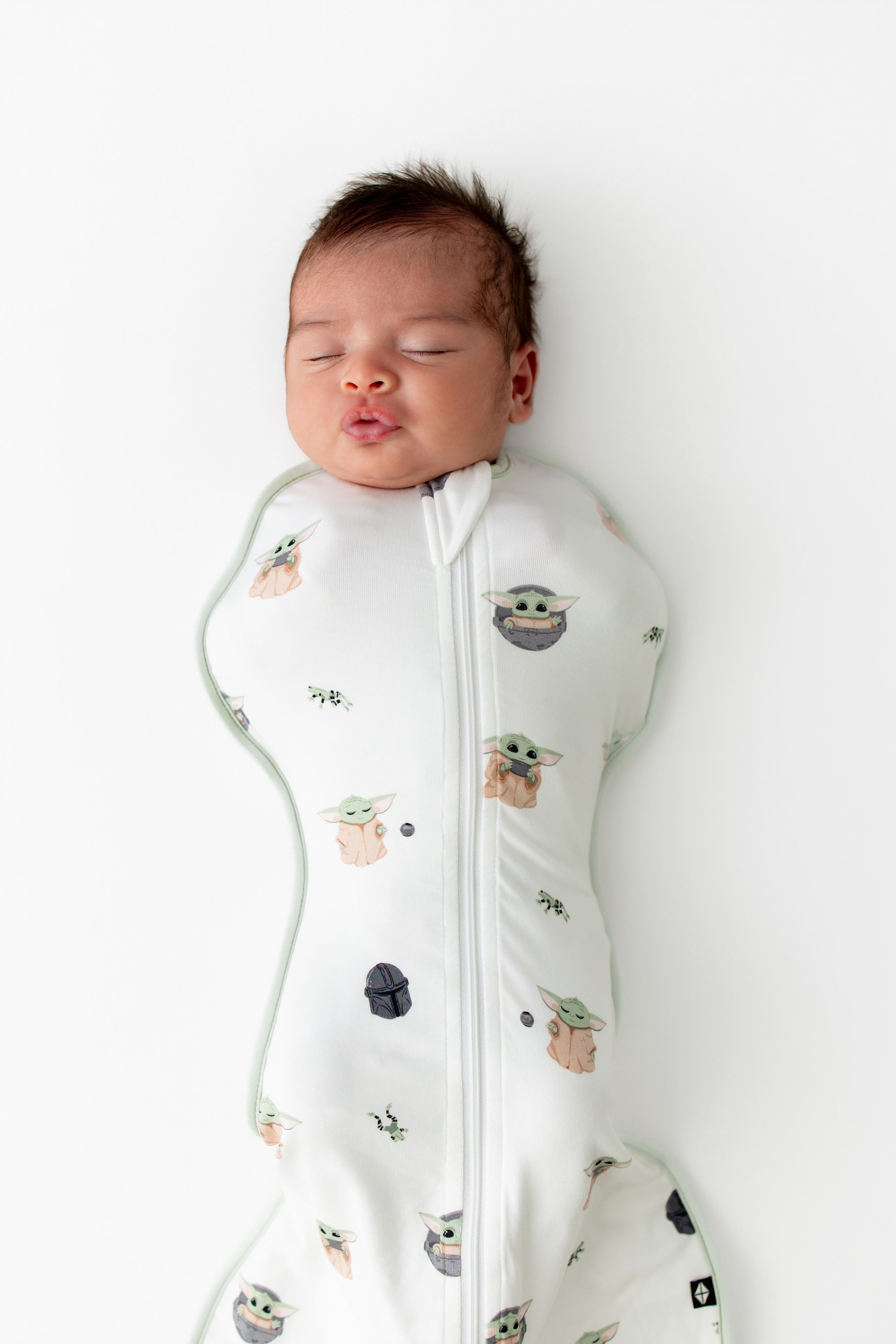 Sleeping newborn wearing the Swaddle Bag in Grogu™ 0.5 laying on a white surface