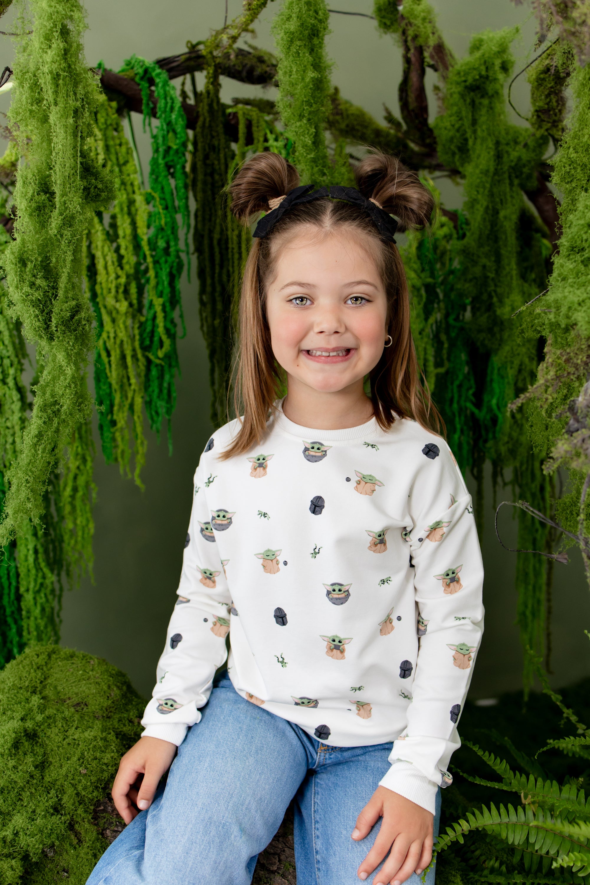 Young smiling girl posing in front of greenery wearing the Sweatshirt in Grogu™