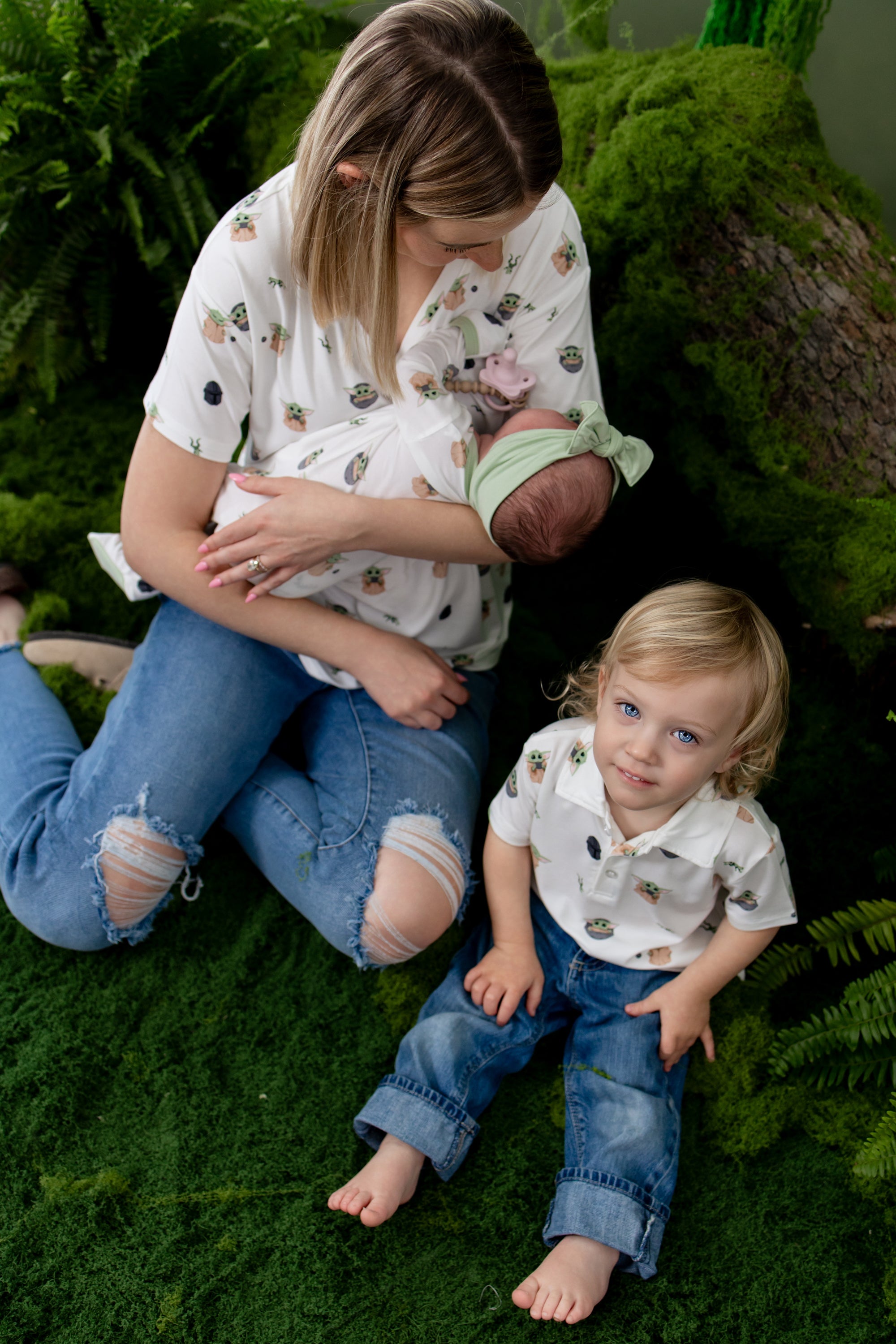 Young boy sitting on greenery wearing the Toddler Short Sleeve Polo in Grogu™ with his mom and baby sister wearing various items in Grogu™