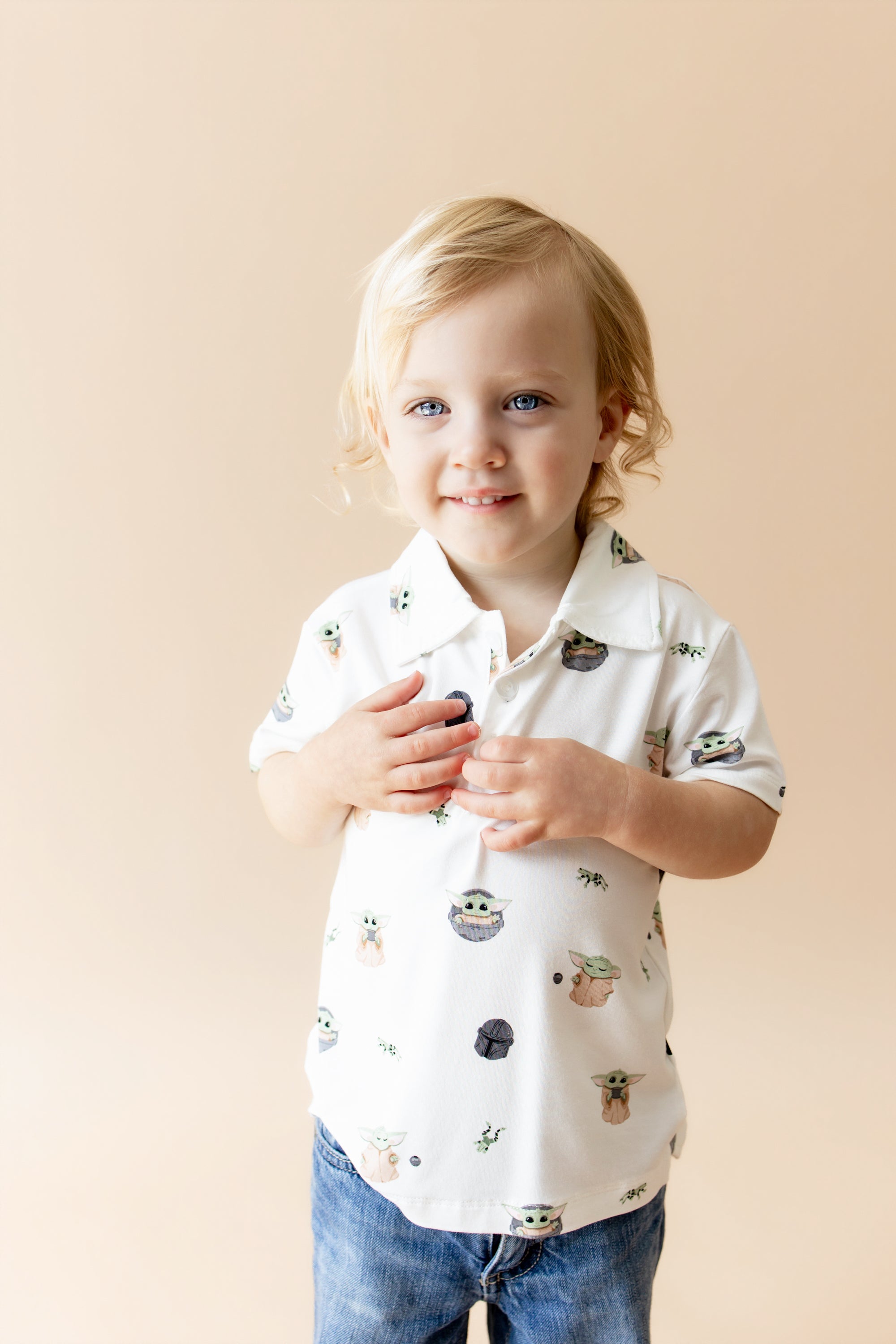 Young child modeling the Toddler Short Sleeve Polo in Grogu™ with medium wash jeans in front of a taupe background