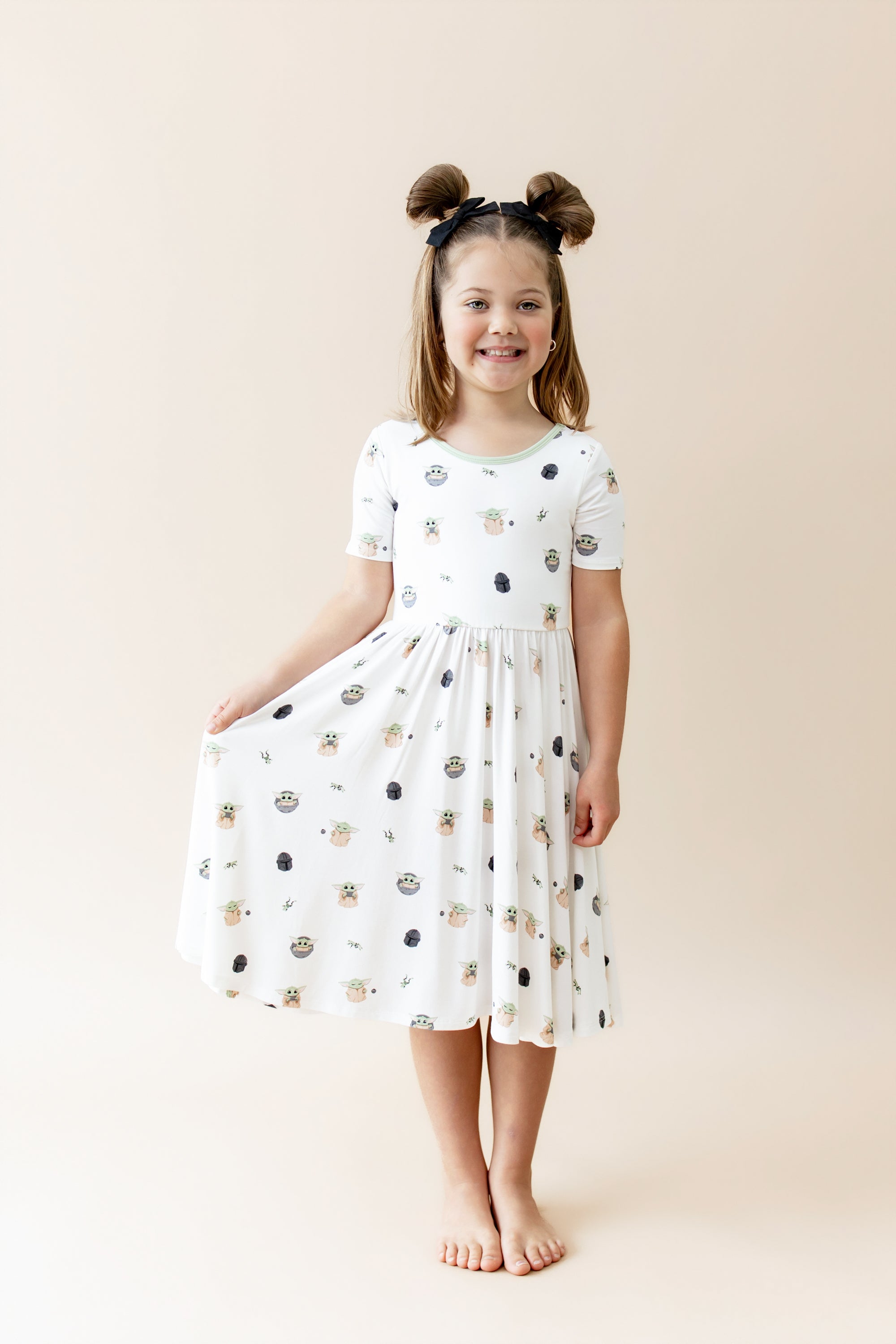 Young girl modeling the Twirl Dress in Grogu™ holding the skirt of the dress out at her side