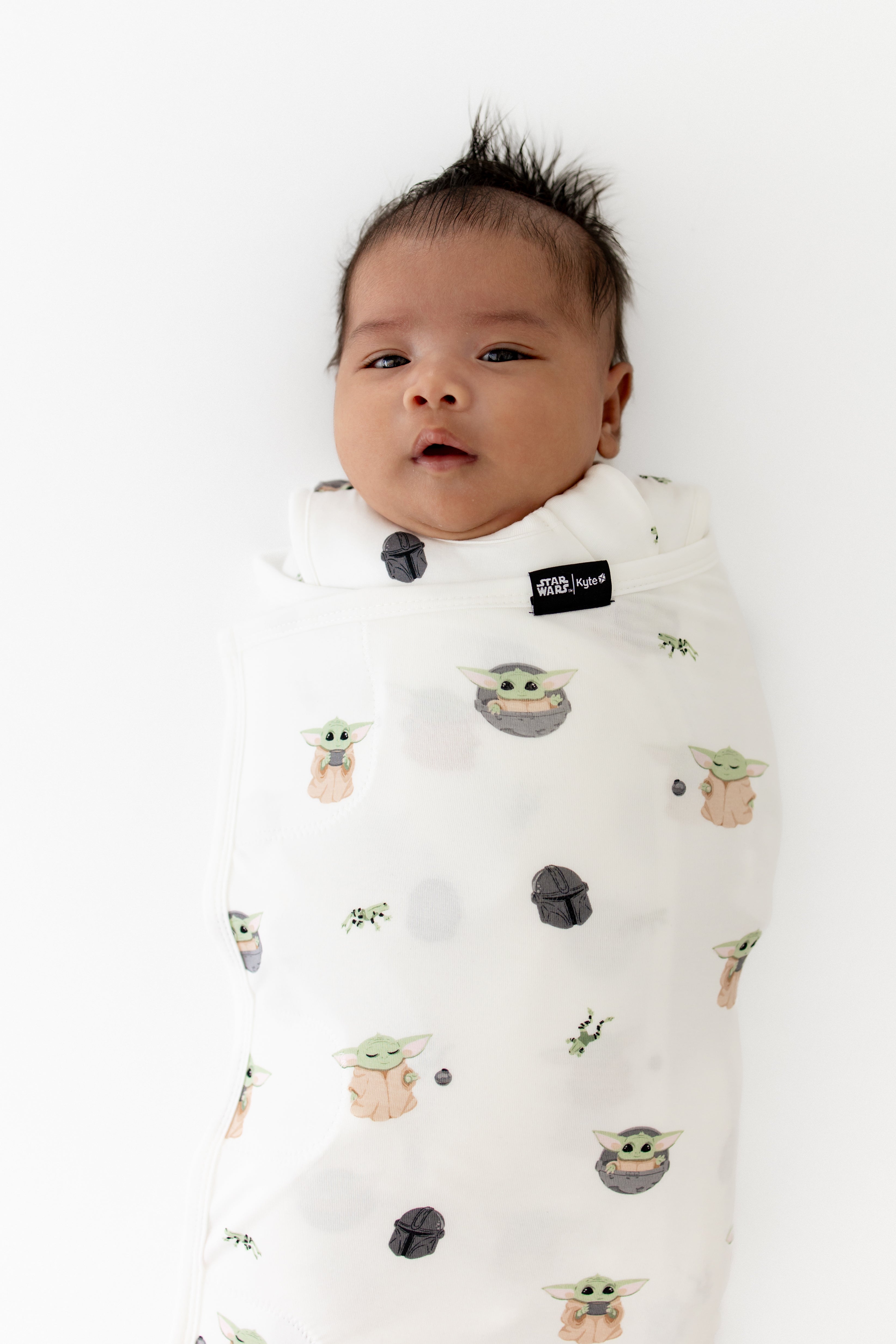 Close up of a newborn swaddled in the Sleep Bag Swaddler in Grogu™ 1.0 showing the black kyte baby logo tag