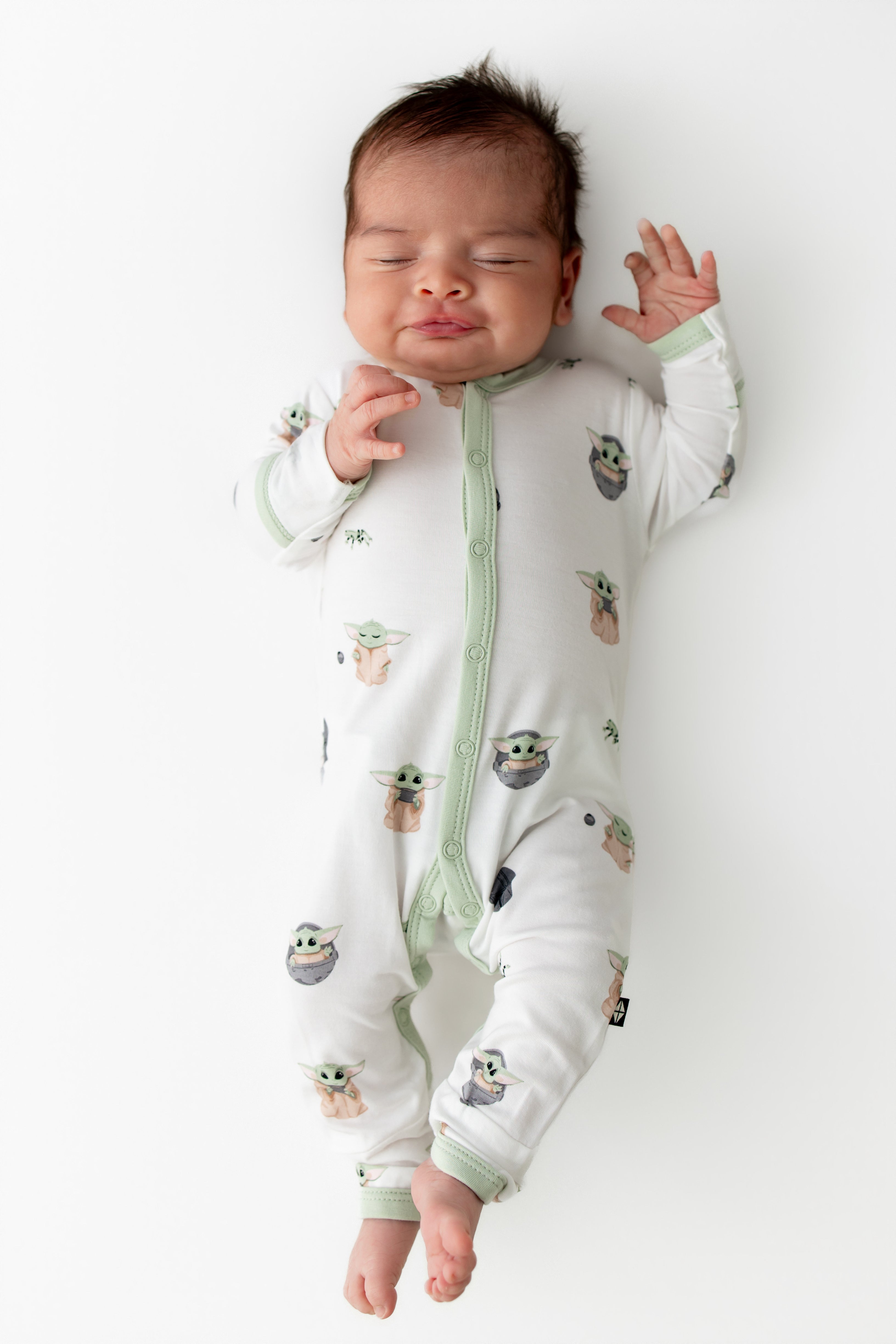 Sleeping newborn wearing the Romper in Grogu™ laying on a white surface