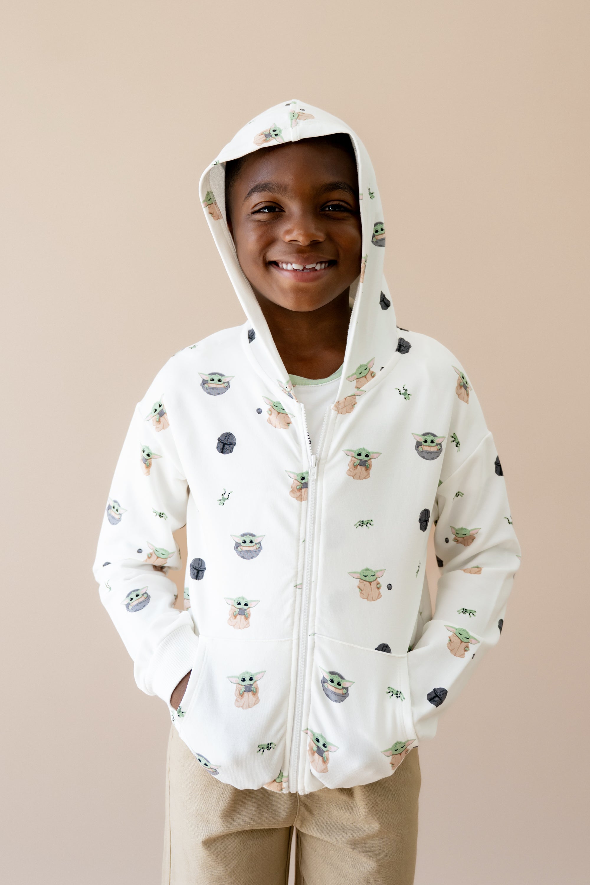 Young boy wearing the Zip-Up Hoodie in Grogu™ with the hood up and his hands in the pockets