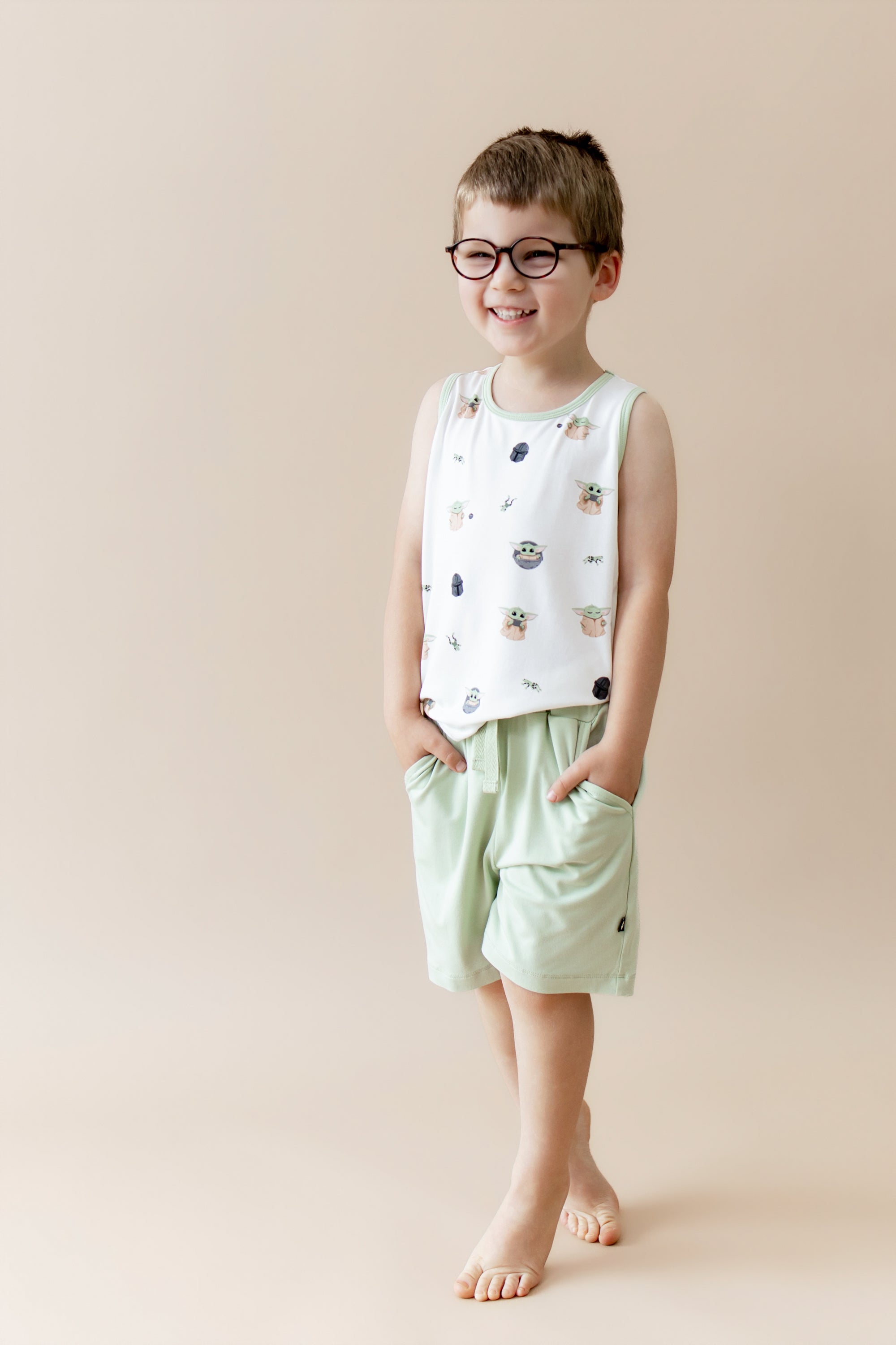 Young boy walking wearing the Toddler Tank Top in Grogu™ with his hands in the pockets of the light green shorts