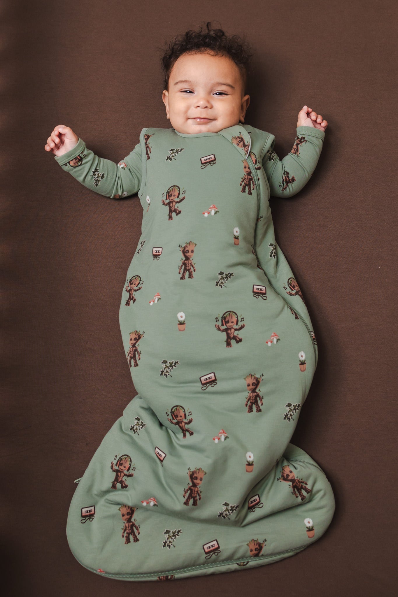 Baby wearing Green Sleep Bag in Groot 1.0 lying on a brown background