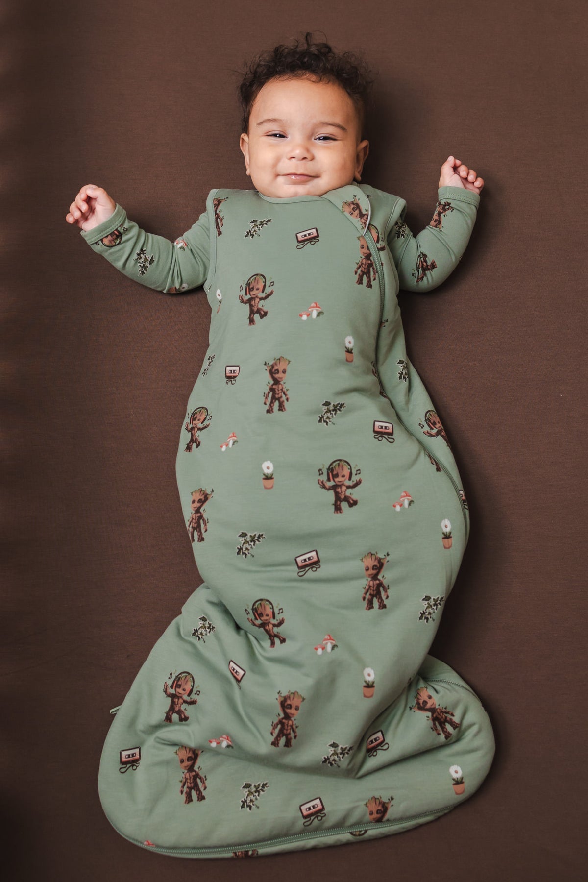 Baby wearing Green Sleep Bag in Groot 1.0 lying on a brown background
