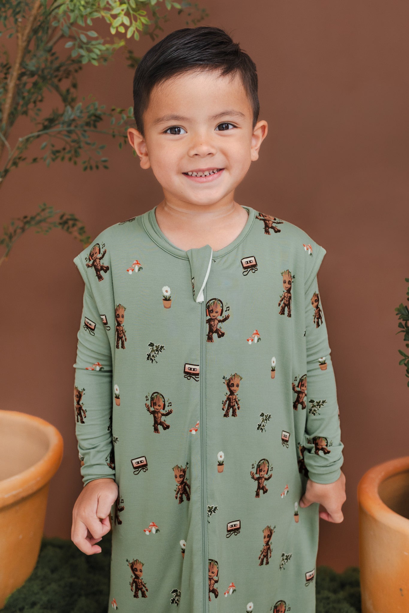 Boy wearing Green Sleep Bag Walker in Groot 1.0 print standing between green plant pots