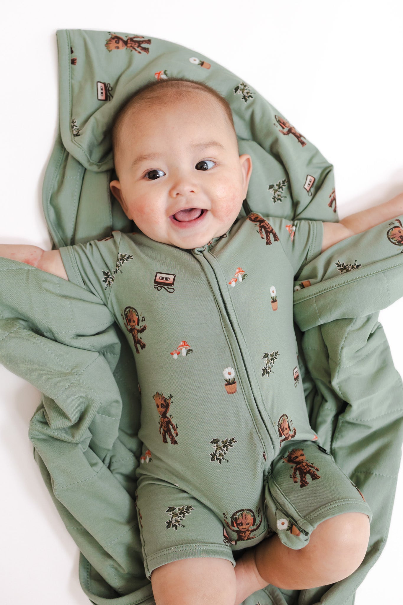 Baby lying over Green Baby Blanket in Groot 1.0 print wearing a similar print zipper shortall on a white background