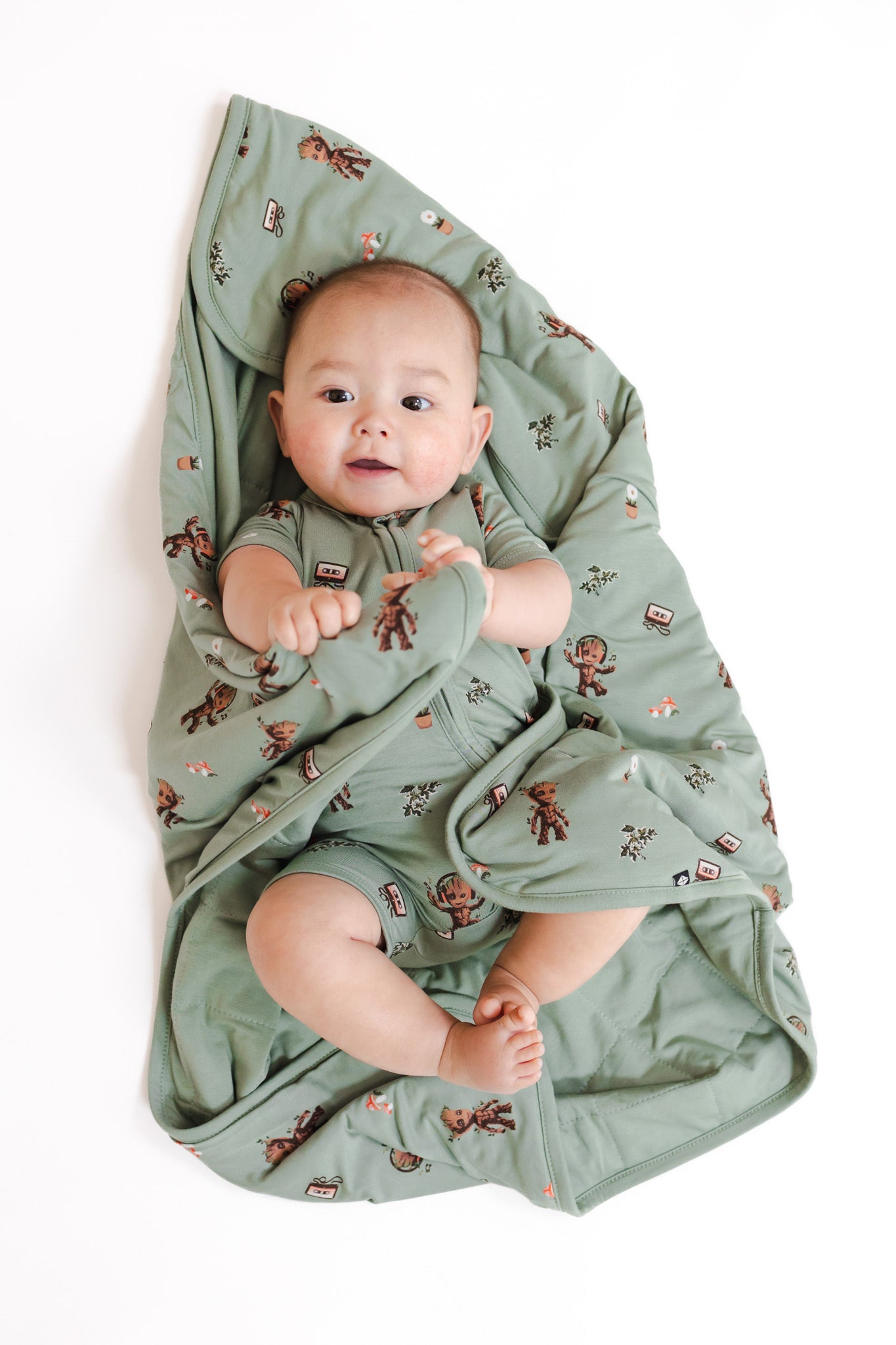 Baby wrapped in Green Baby Blanket in Groot 1.0 print wearing similar print zipper shortall on a white background