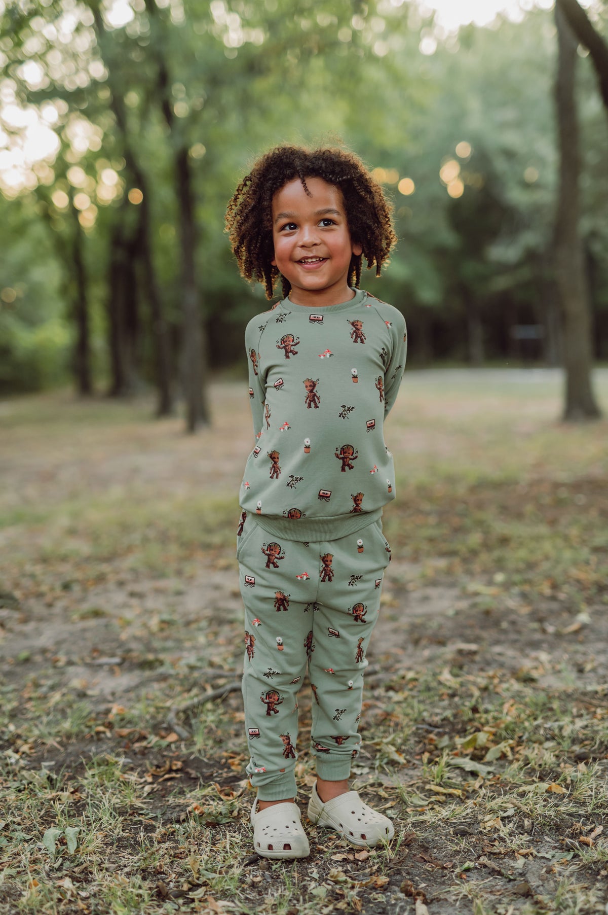 boy outside with his hands behind his back wearing groot jogger set and smiling.