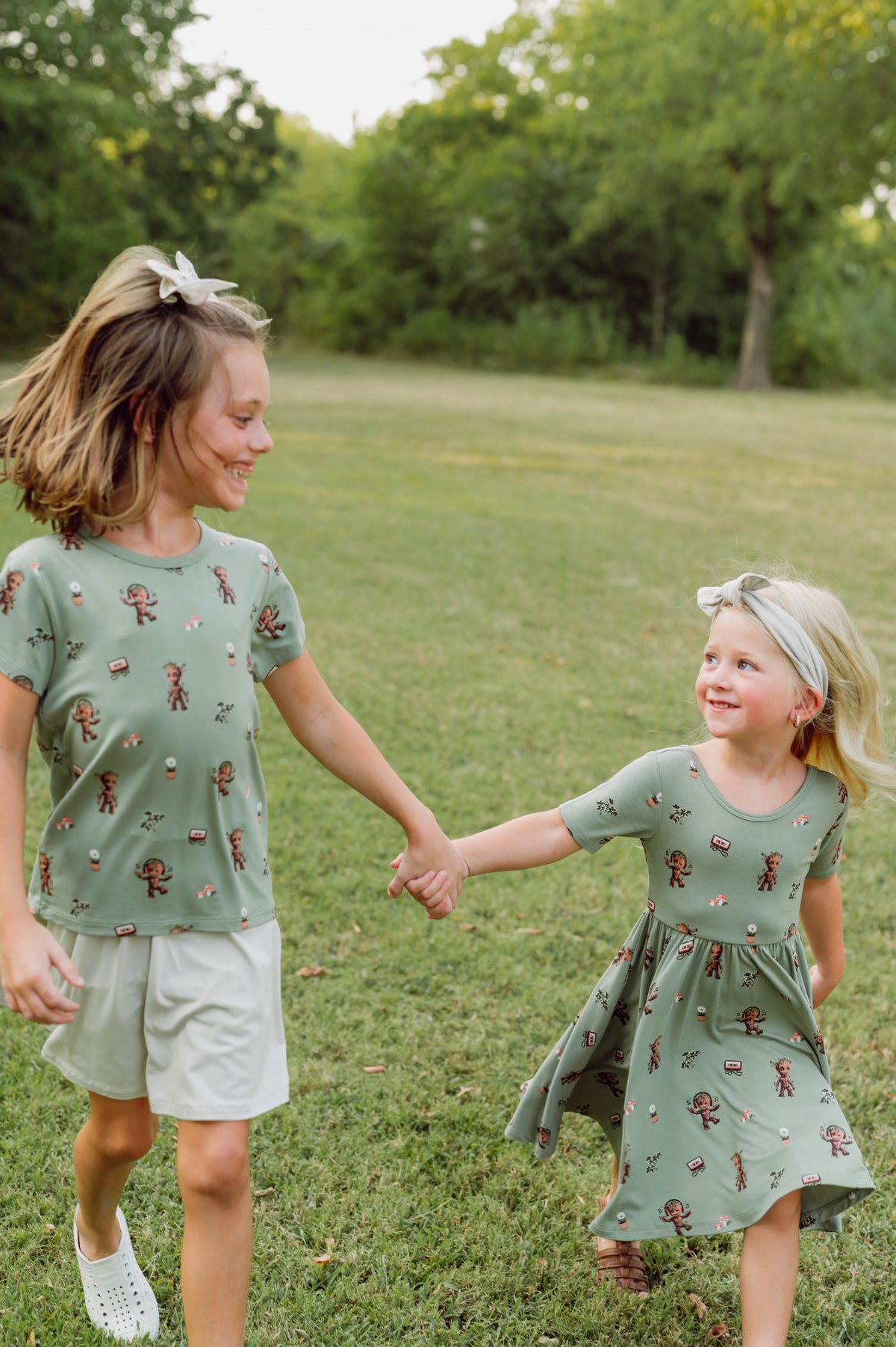 Two girls walking in grass wearing Twirl Dress and toddler basic tee in Groot print