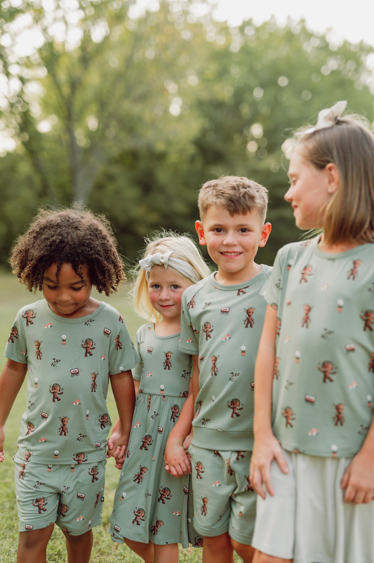 Two boys and two girls standing together outdoors in forest wearing Short Sleeve Jogger Set, toddler basic tee over drawstring shorts and twirl dress in Groot print