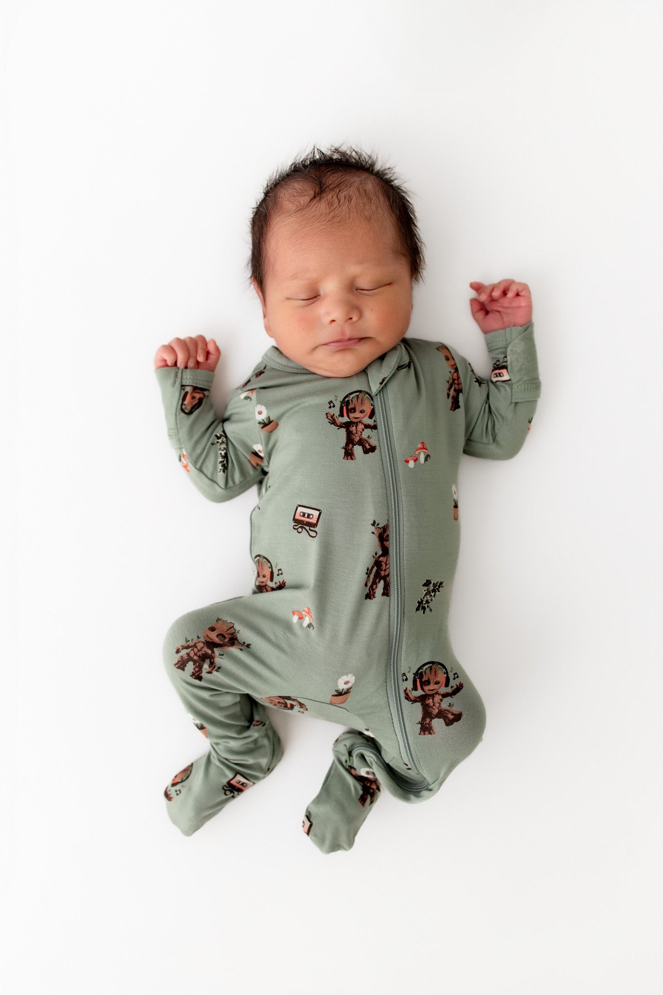 Baby sleeping wearing Green Zippered Footie in Groot print on a white background