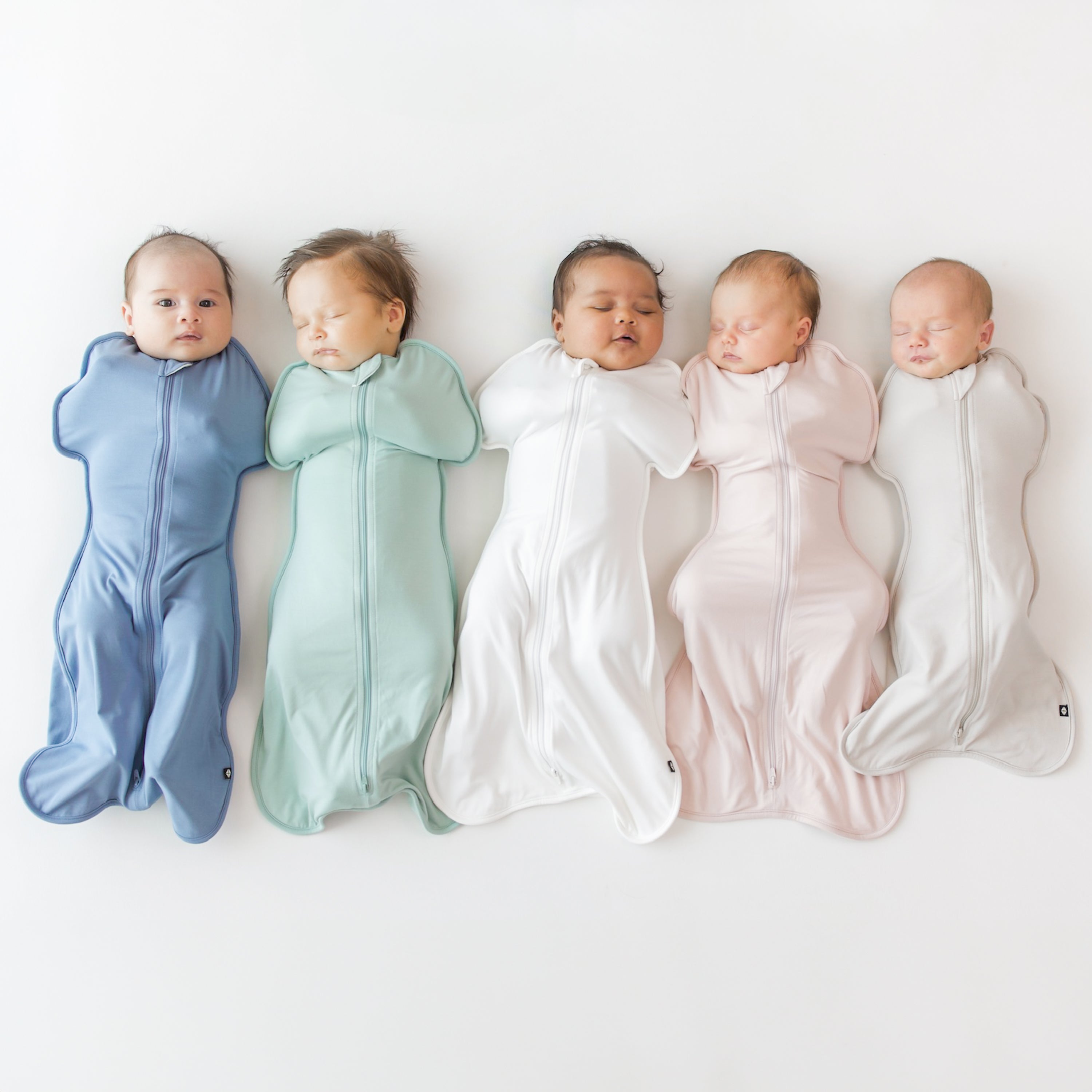 Group of 5 babies in Kyte Baby Swaddle Bags in colors slate, sage, cloud, blush and oat
