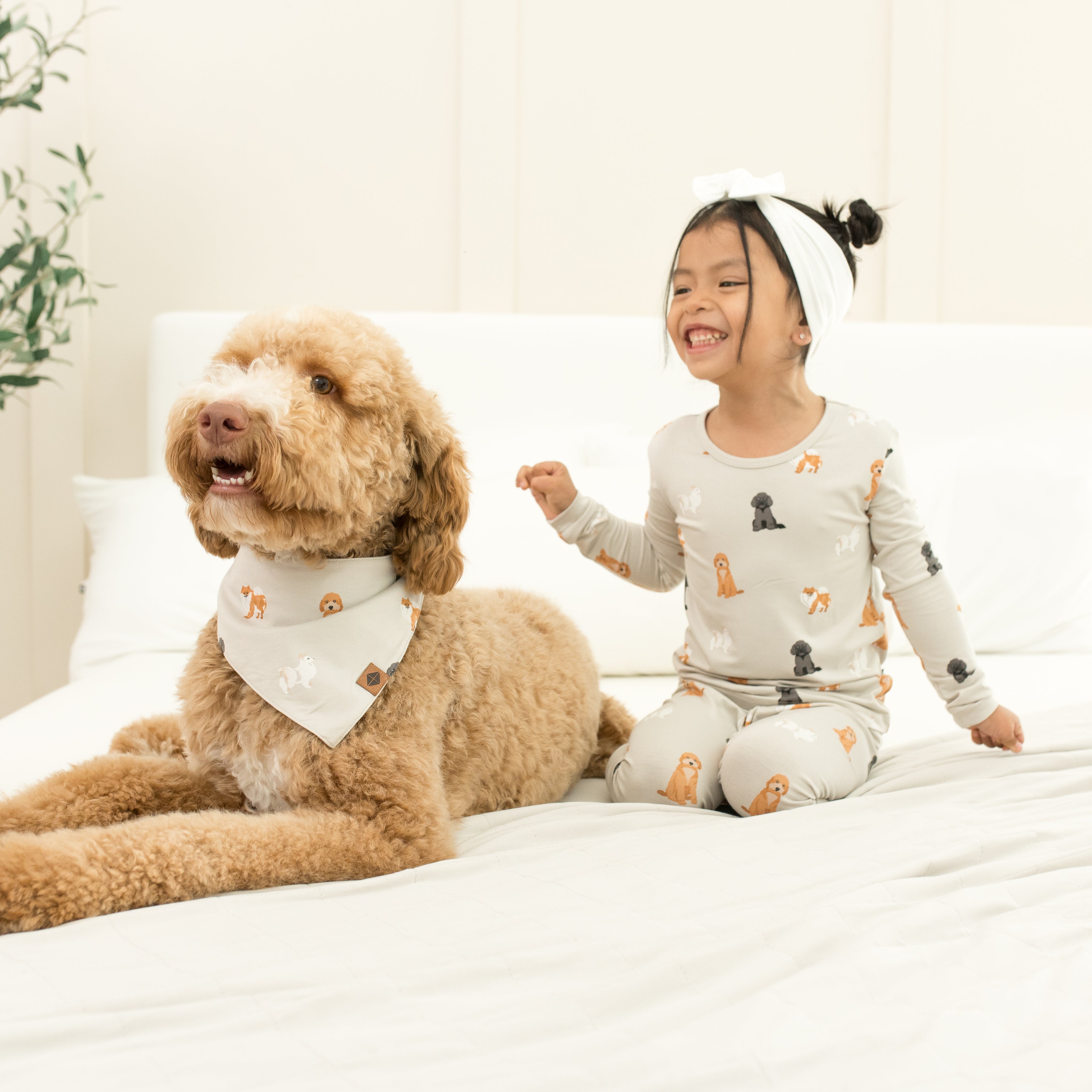 Toddler wearing Long Sleeve Pajamas in Fluffy Dog on a bed next to a dog with matching bandana
