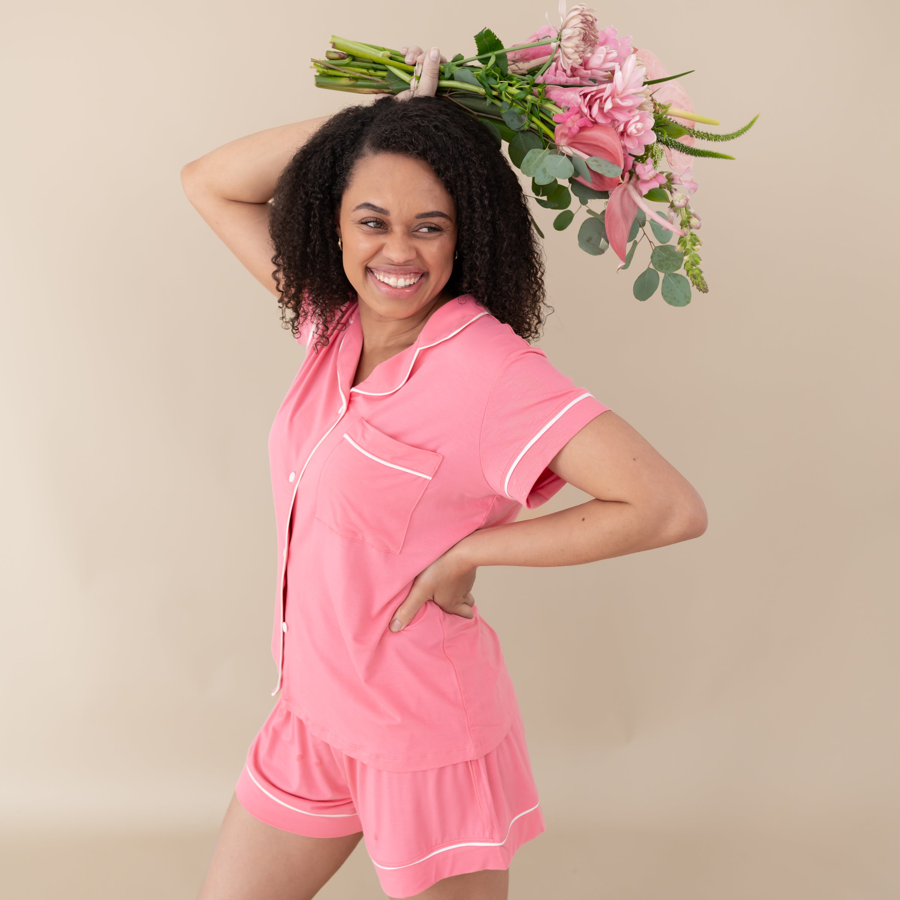Woman modeling Women’s Short Sleeve Pajama Set in Guava with Cloud Trim holding a bouquet of flowers above head