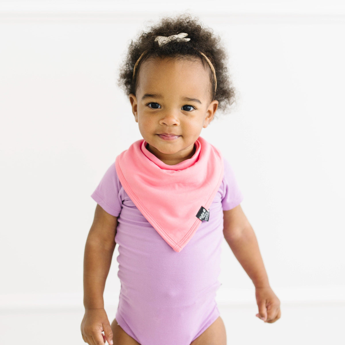 Toddler wearing short sleeve bodysuit in poi with pink guava bib