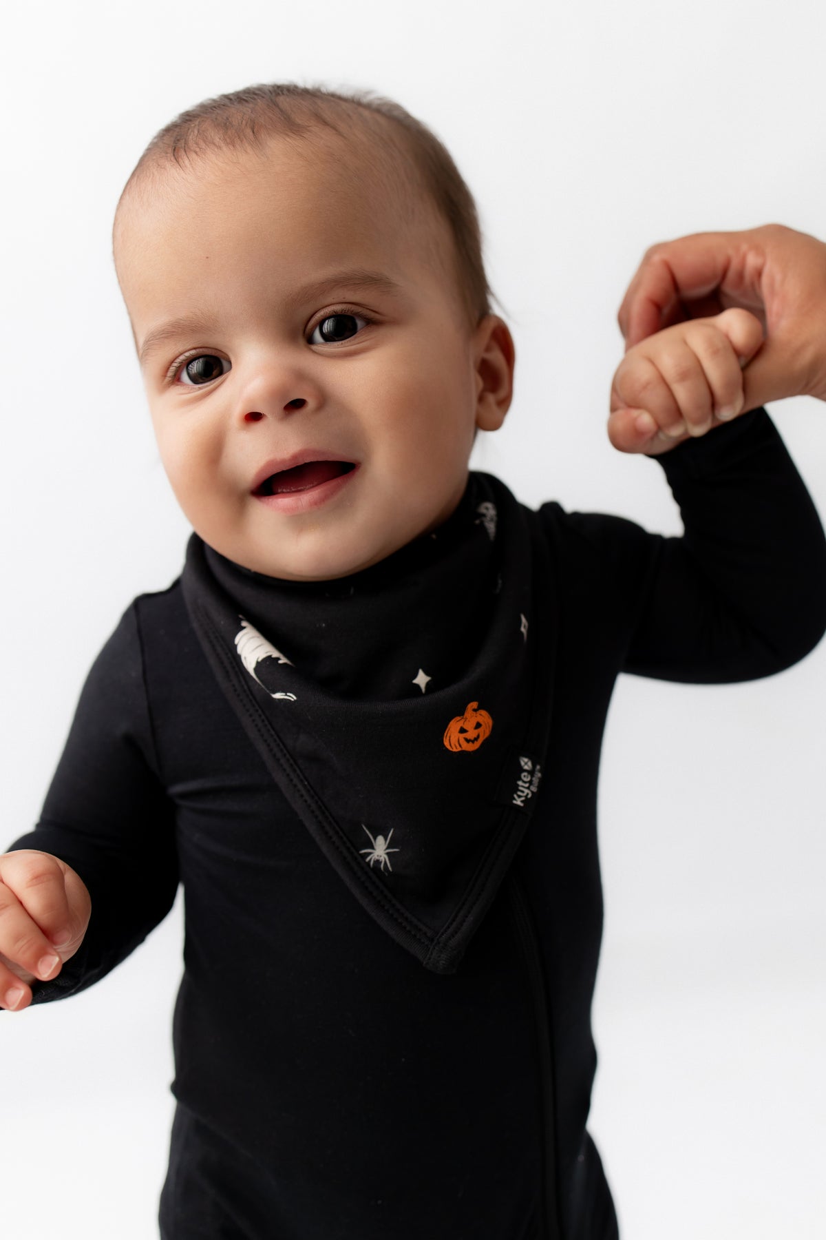 Baby wearing Bib in Halloween Friends print over a black romper holding a hand on a white background