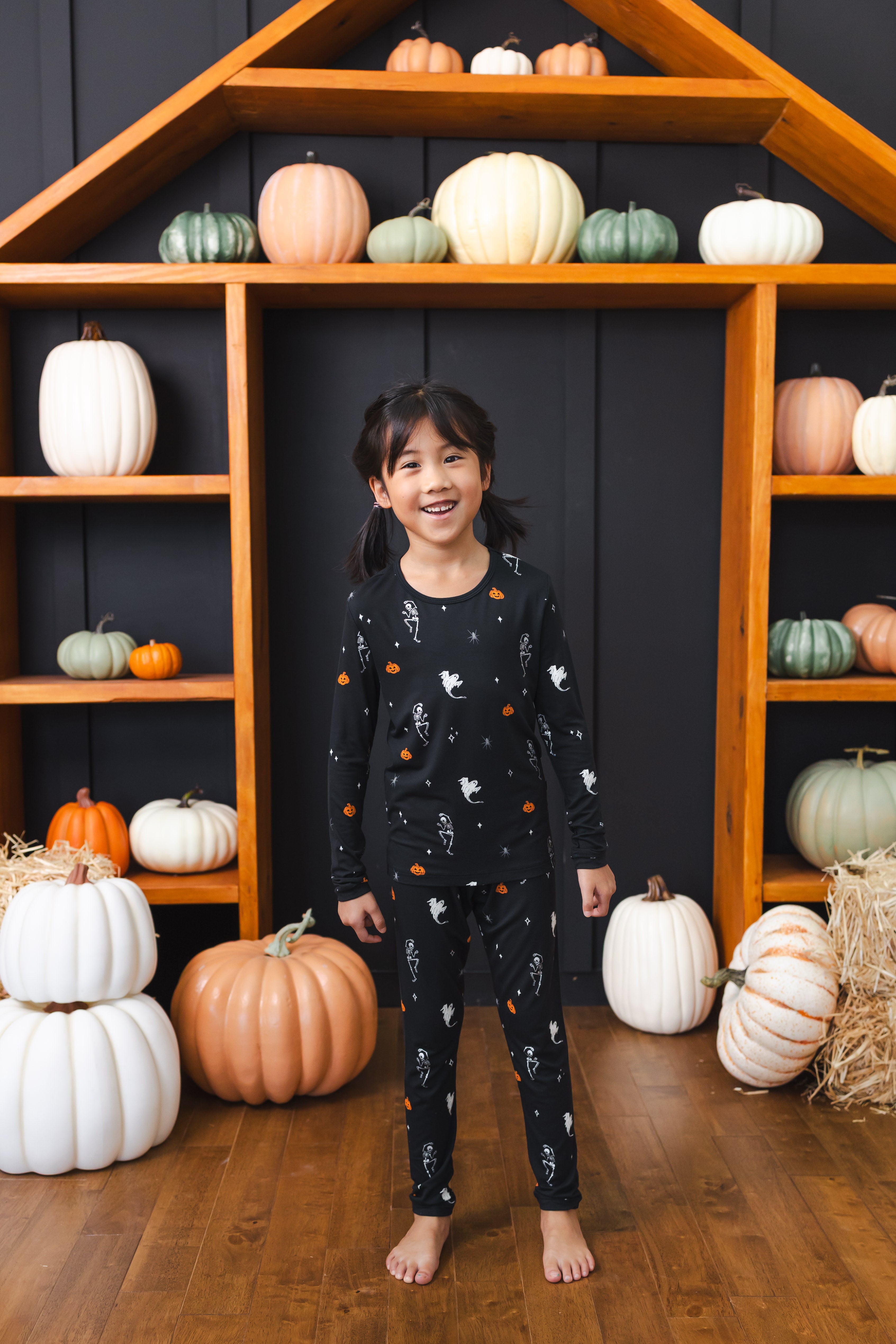 Girl wearing black Long Sleeve Pajamas in Halloween Friends print standing in front of pumpkin decorations