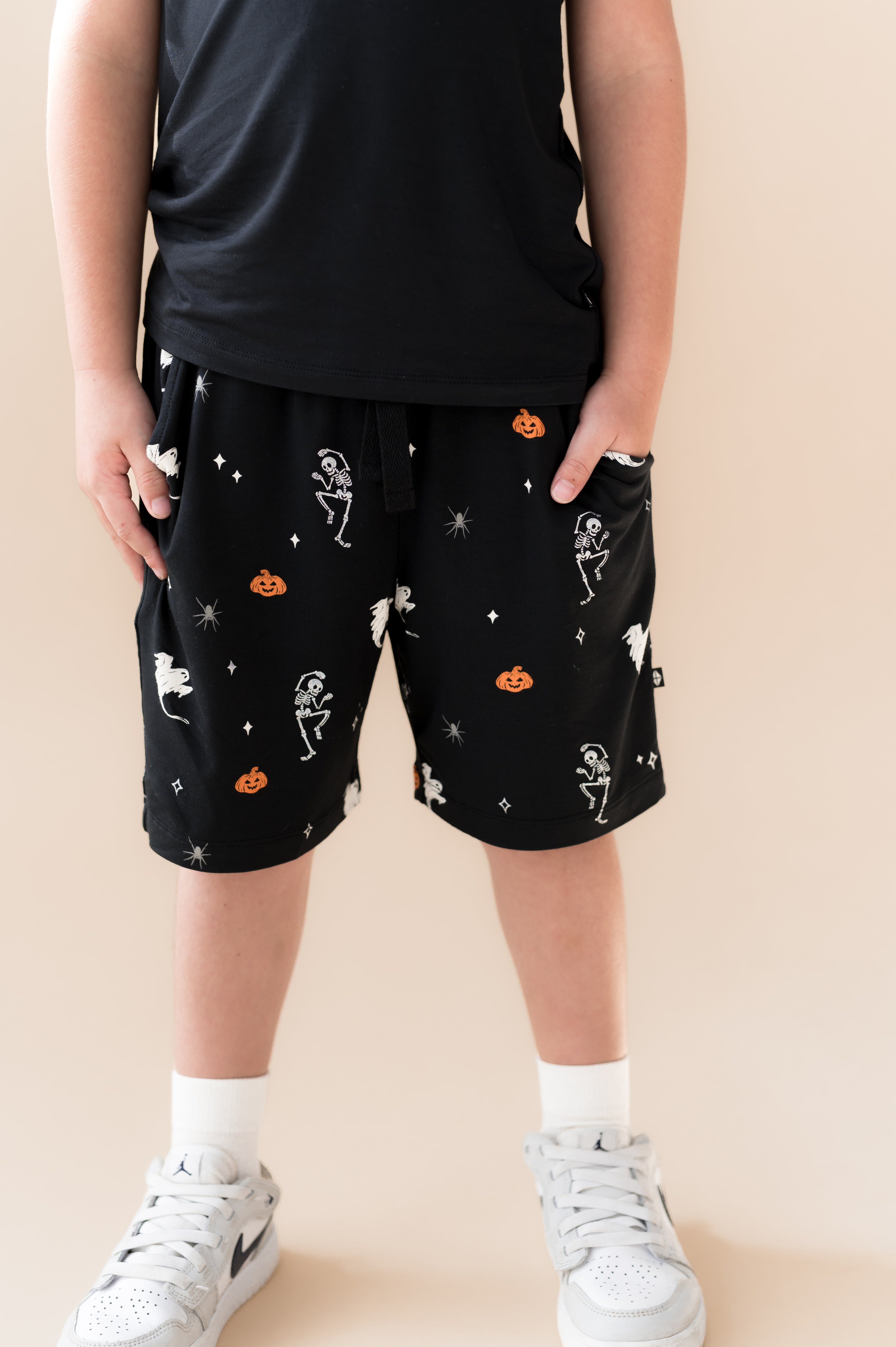Toddler wearing Drawstring Short in Halloween Friends print under Black T-shirt on a beige background