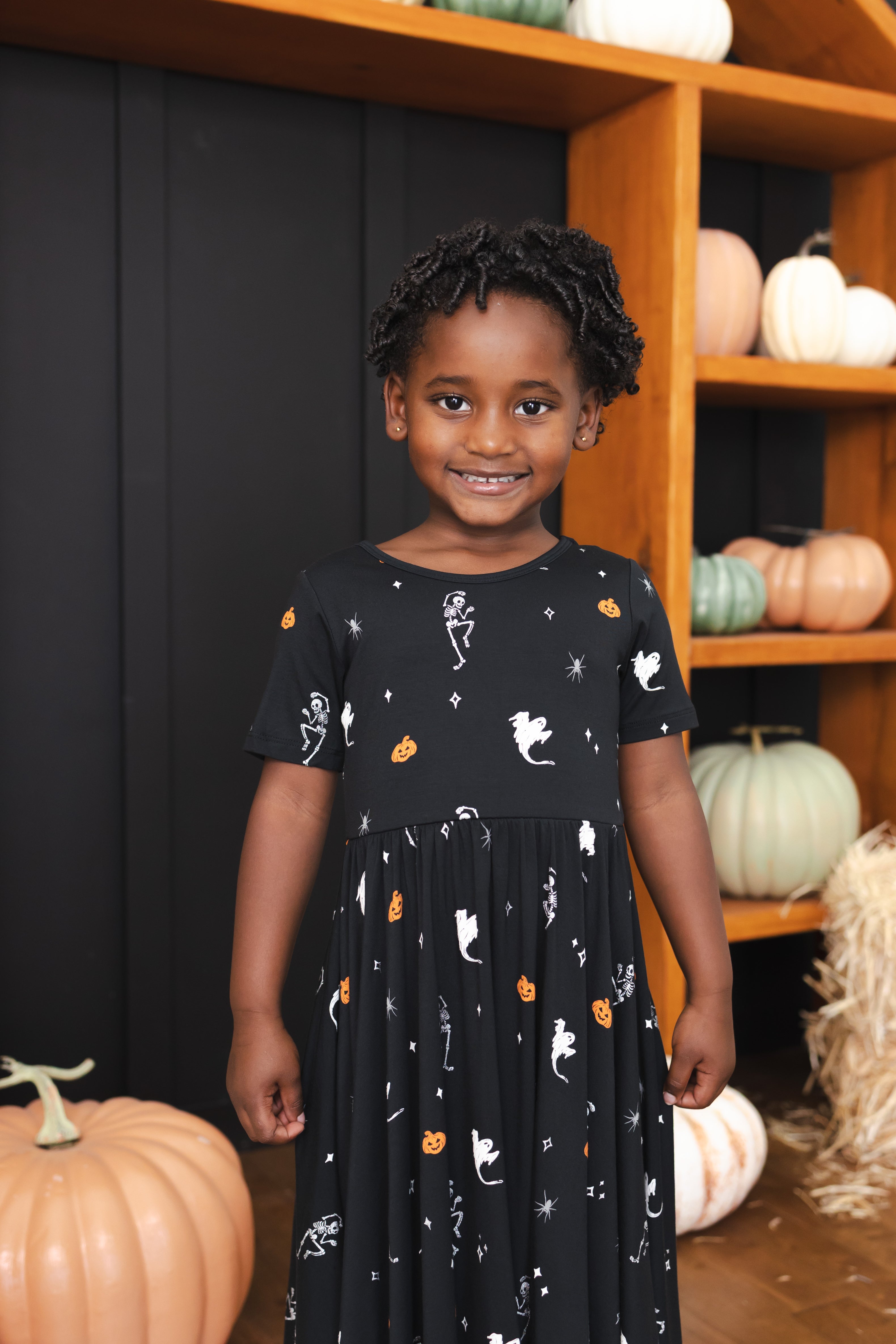 Girl smiling in Twirl Dress in Halloween Friends print standing in front of Halloween decorations