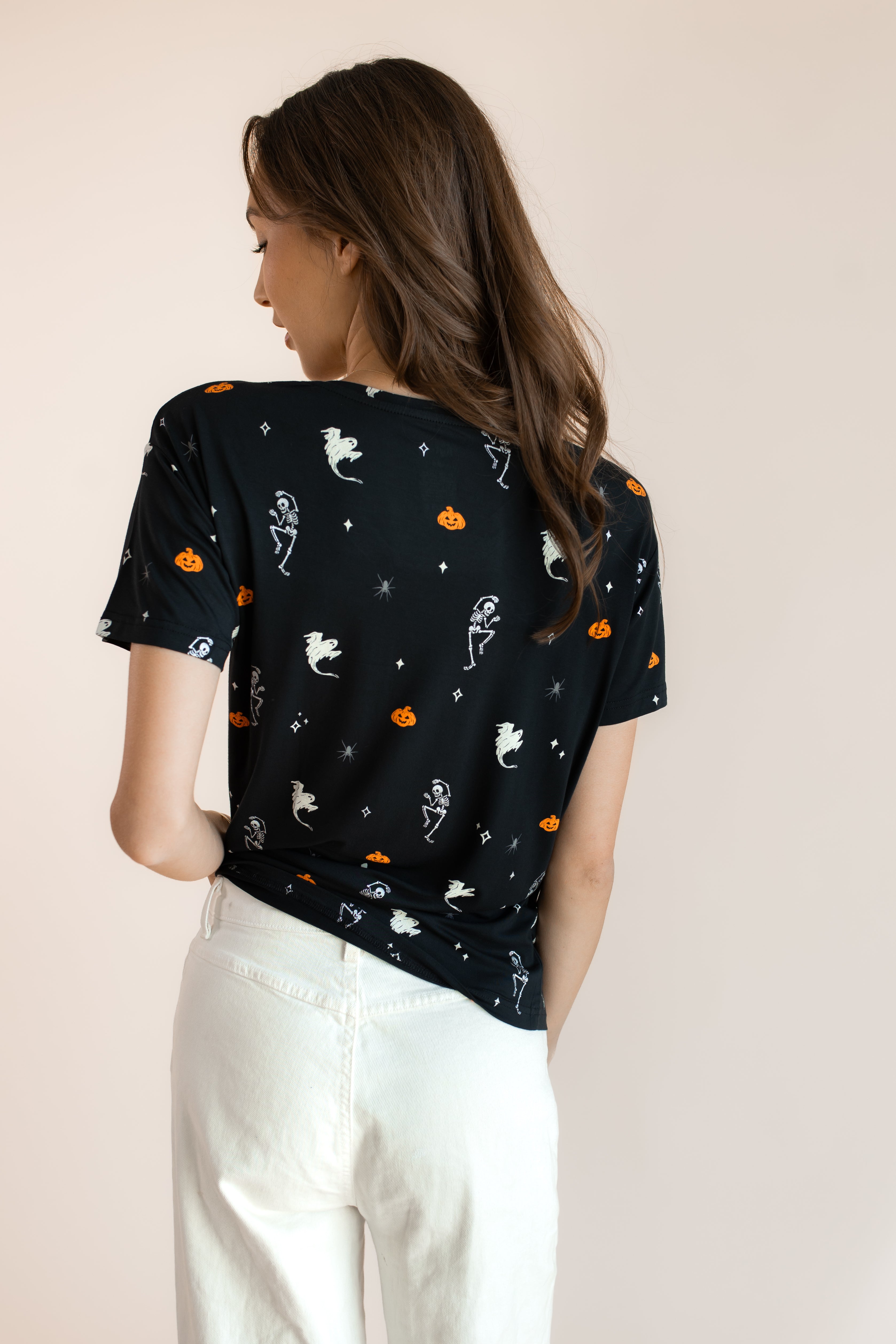 Back side of Modal wearing Women's Oversized V-Neck Tee in Halloween Friends print over white pants on a beige background