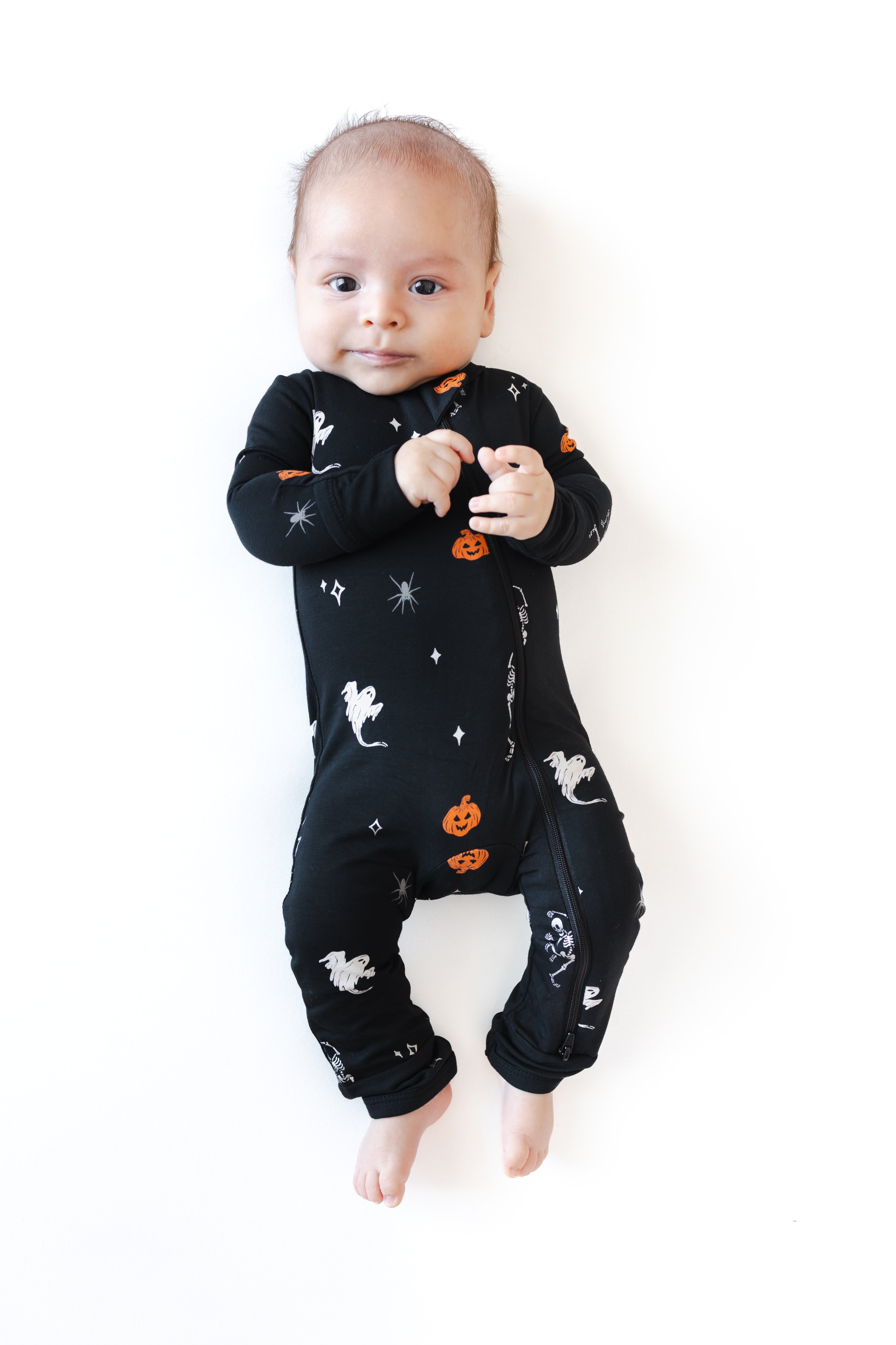 Baby wearing Zippered Romper in Halloween Friends print lying on a white background