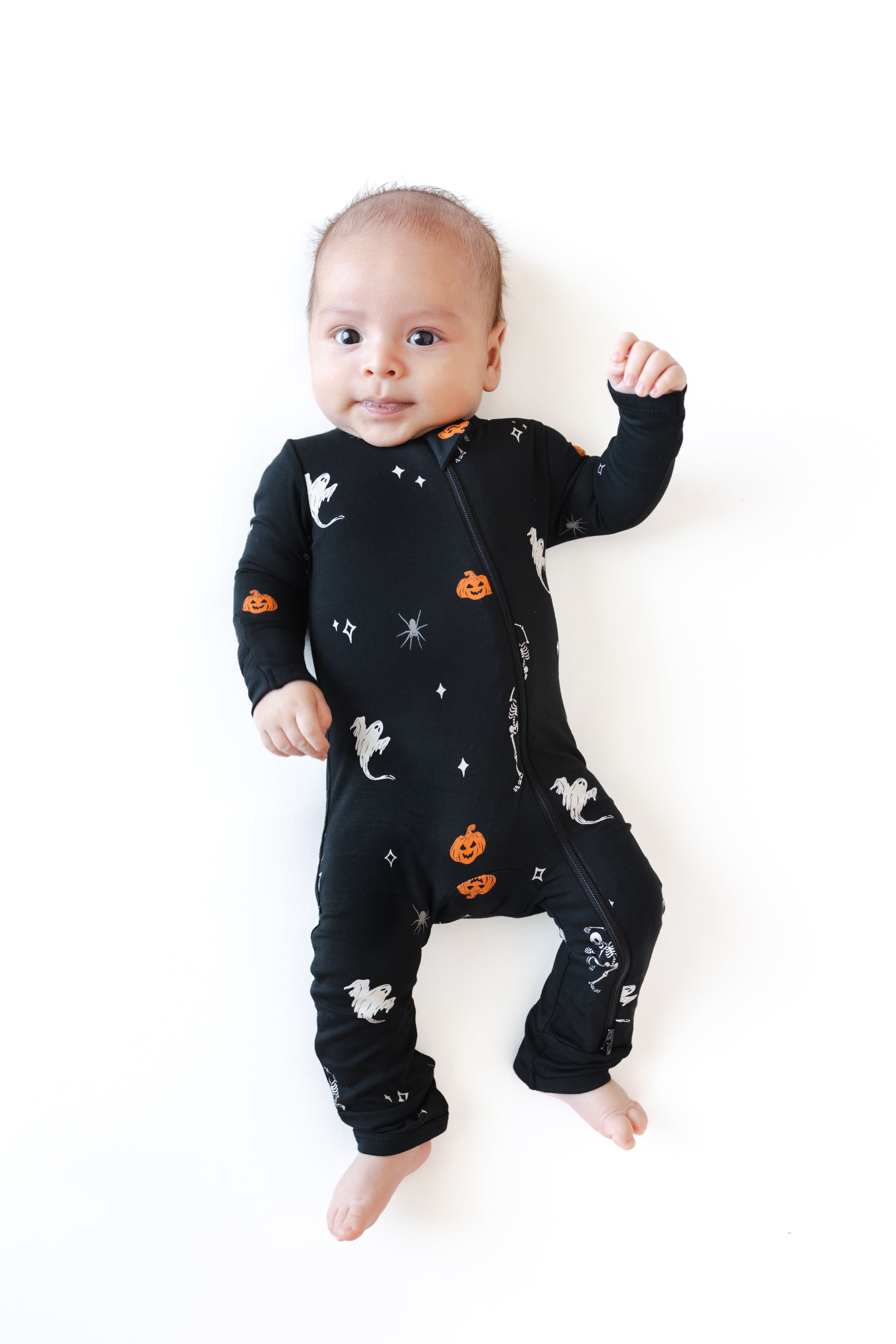 Baby wearing Zippered Romper in Halloween Friends print lying on a white background
