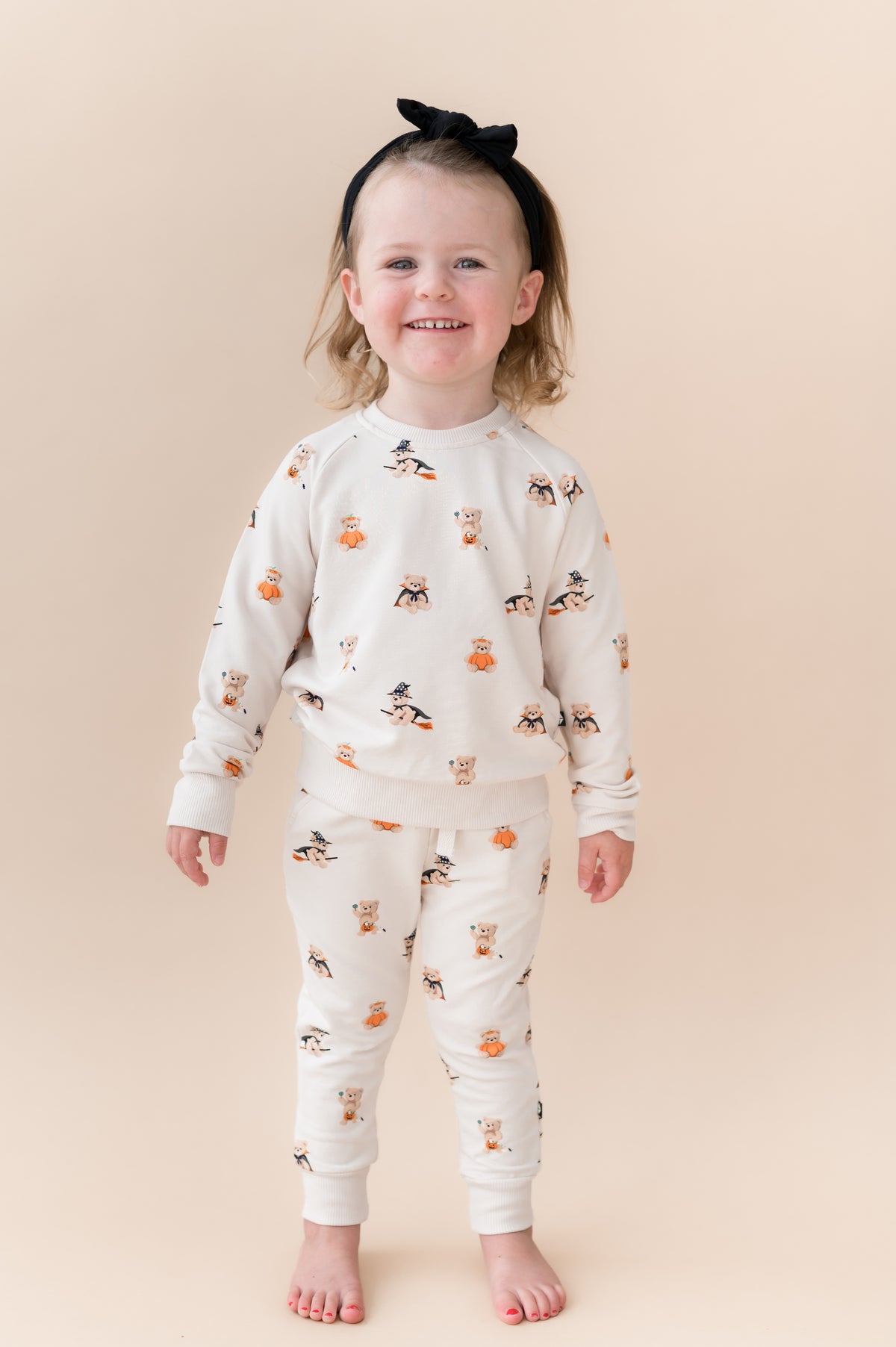 Girl posing in Beige Long Sleeve Jogger Set in Halloween Teddy print with a black bow on a beige background