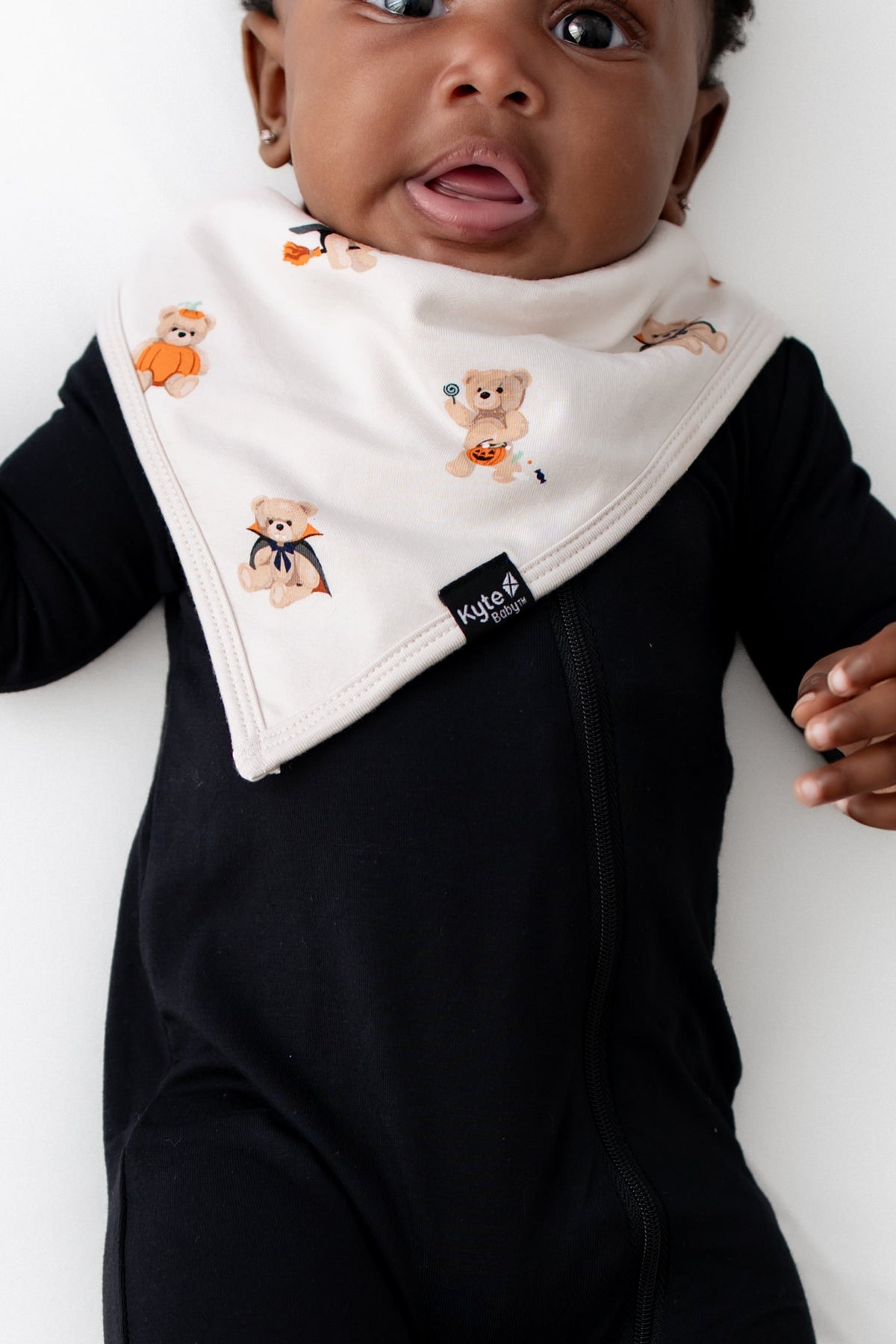 Close up of Baby wearing Bib in Halloween Teddy print over a black romper on a white background