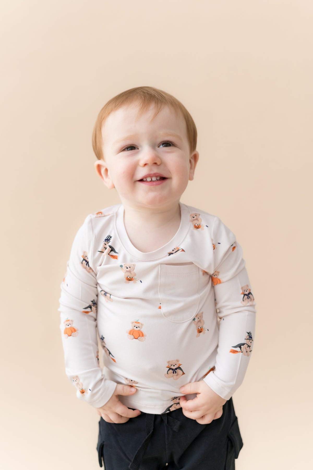 Boy wearing Long Sleeve Toddler Crew Neck Tee in Halloween Teddy print over black shorts on a beige background