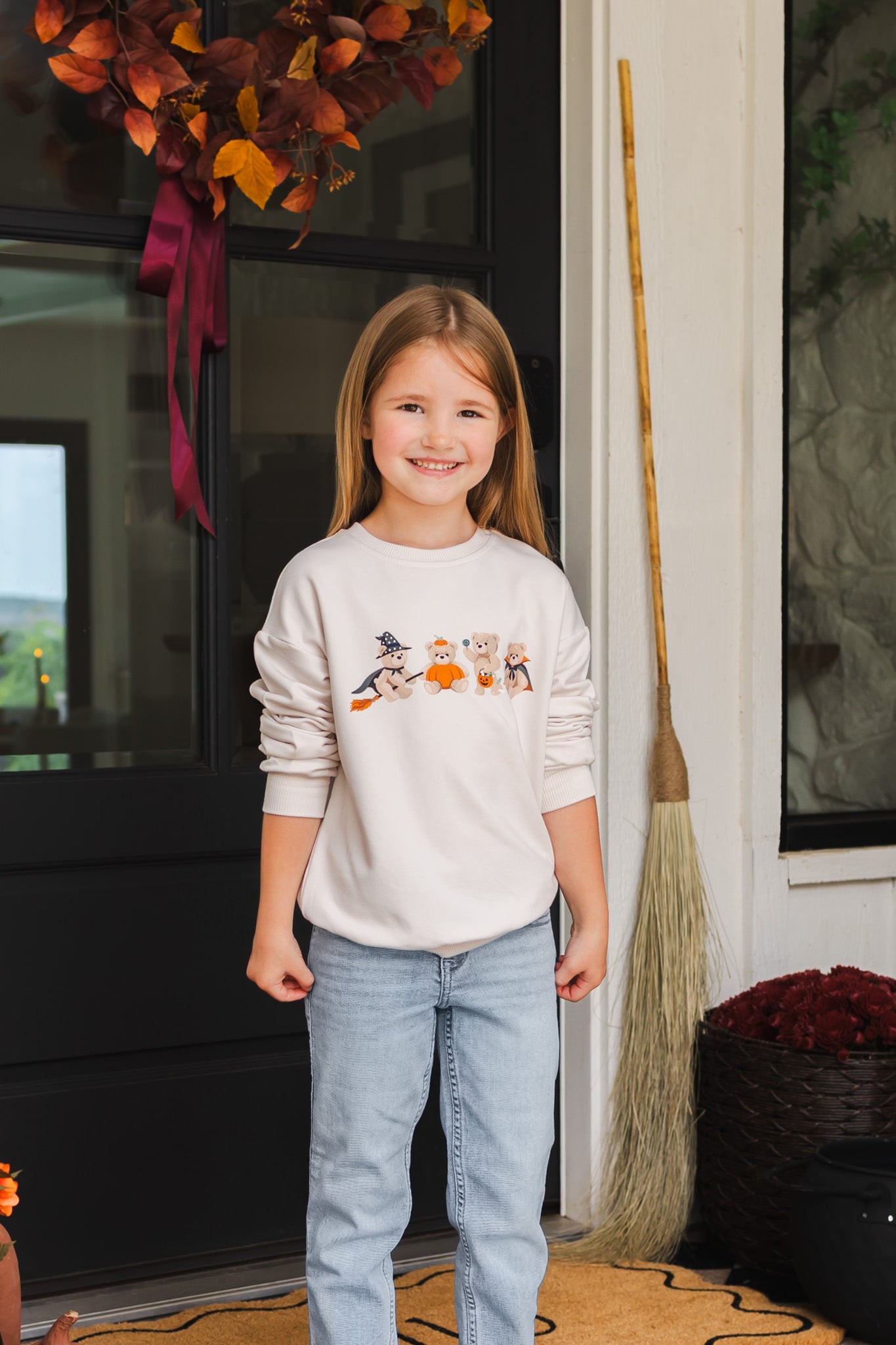 Girl smiling in Beige Sweatshirt with Halloween Teddy print in its center standing outdoors