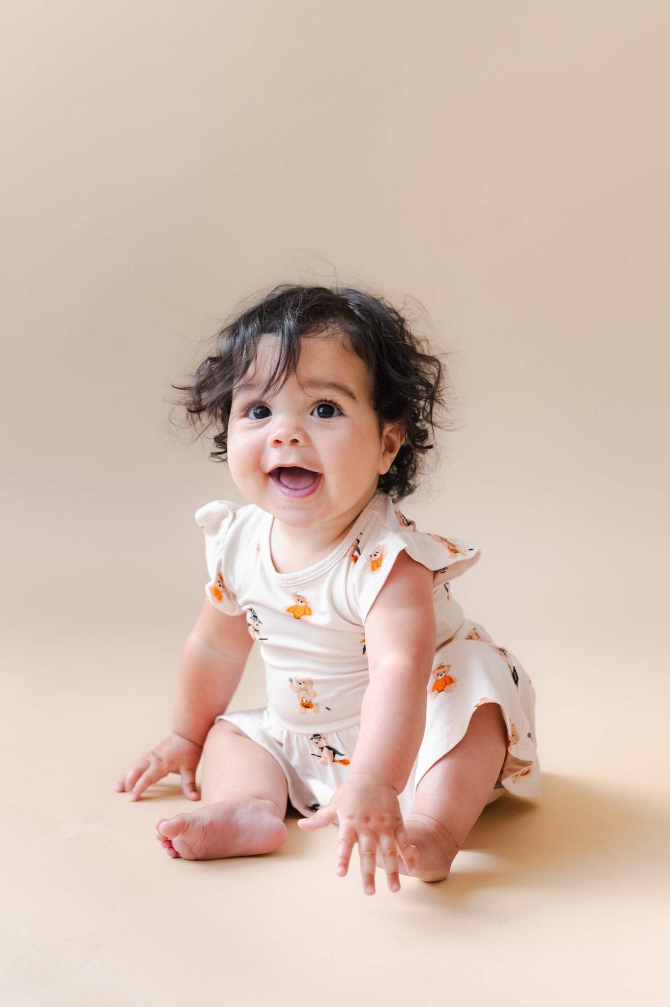 Baby posing in Twirl Bodysuit Dress in Halloween Teddy print on a beige background