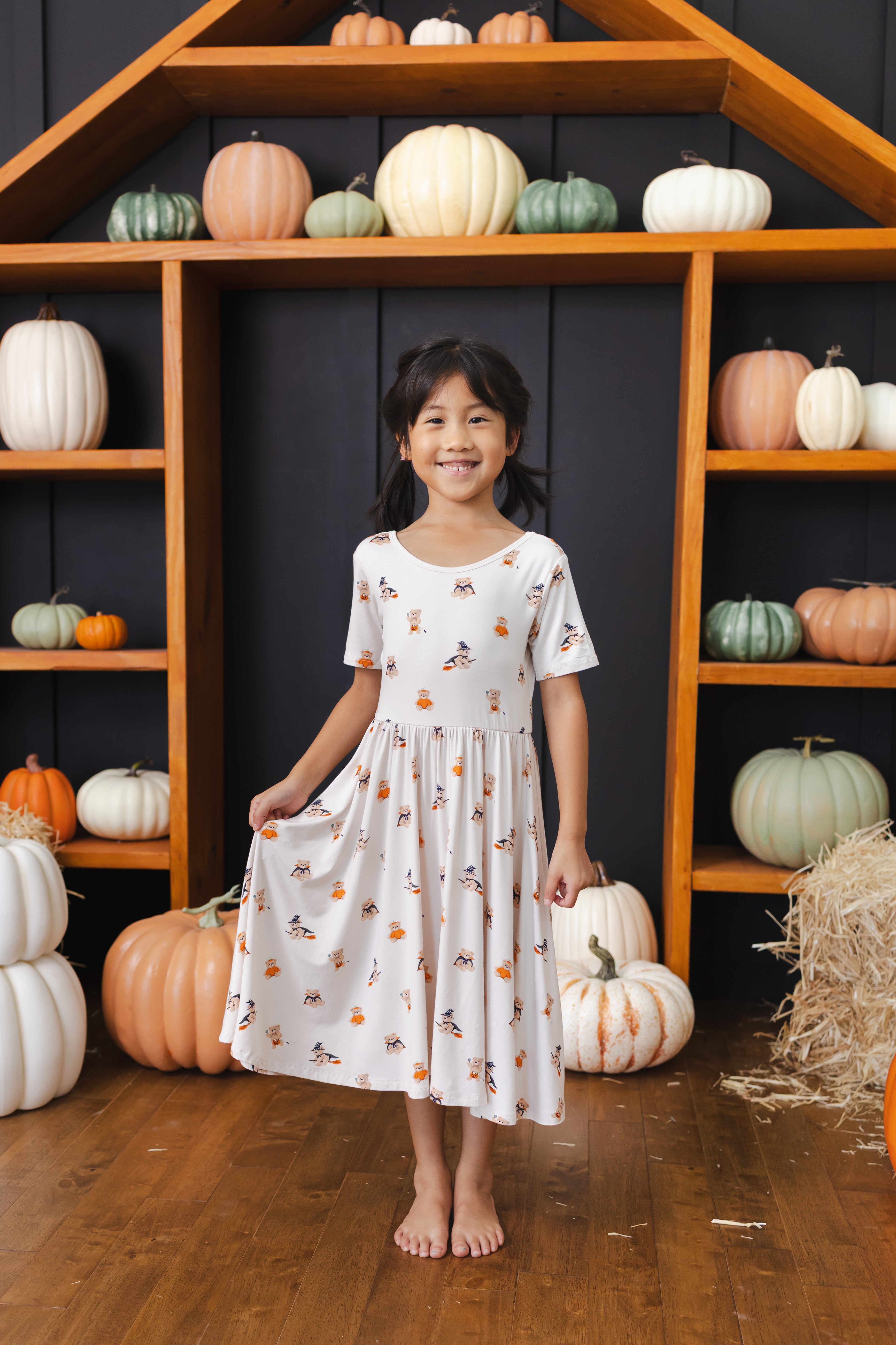 Girl wearing Twirl Dress in Halloween Teddy print standing in front of pumpkin Halloween decorations around
