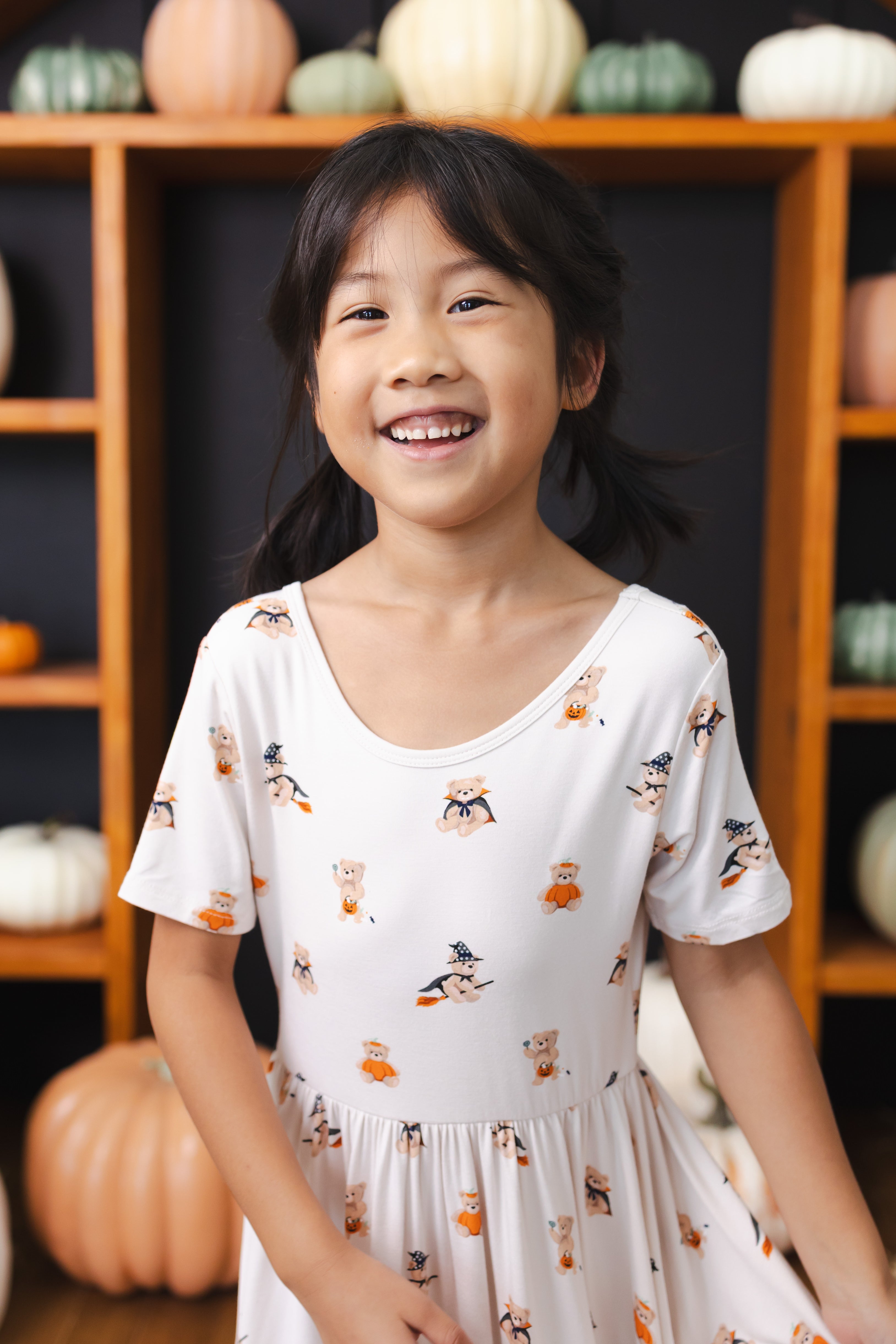 Girl smiling Twirl Dress in Halloween Teddy print with pumpkin decorations around