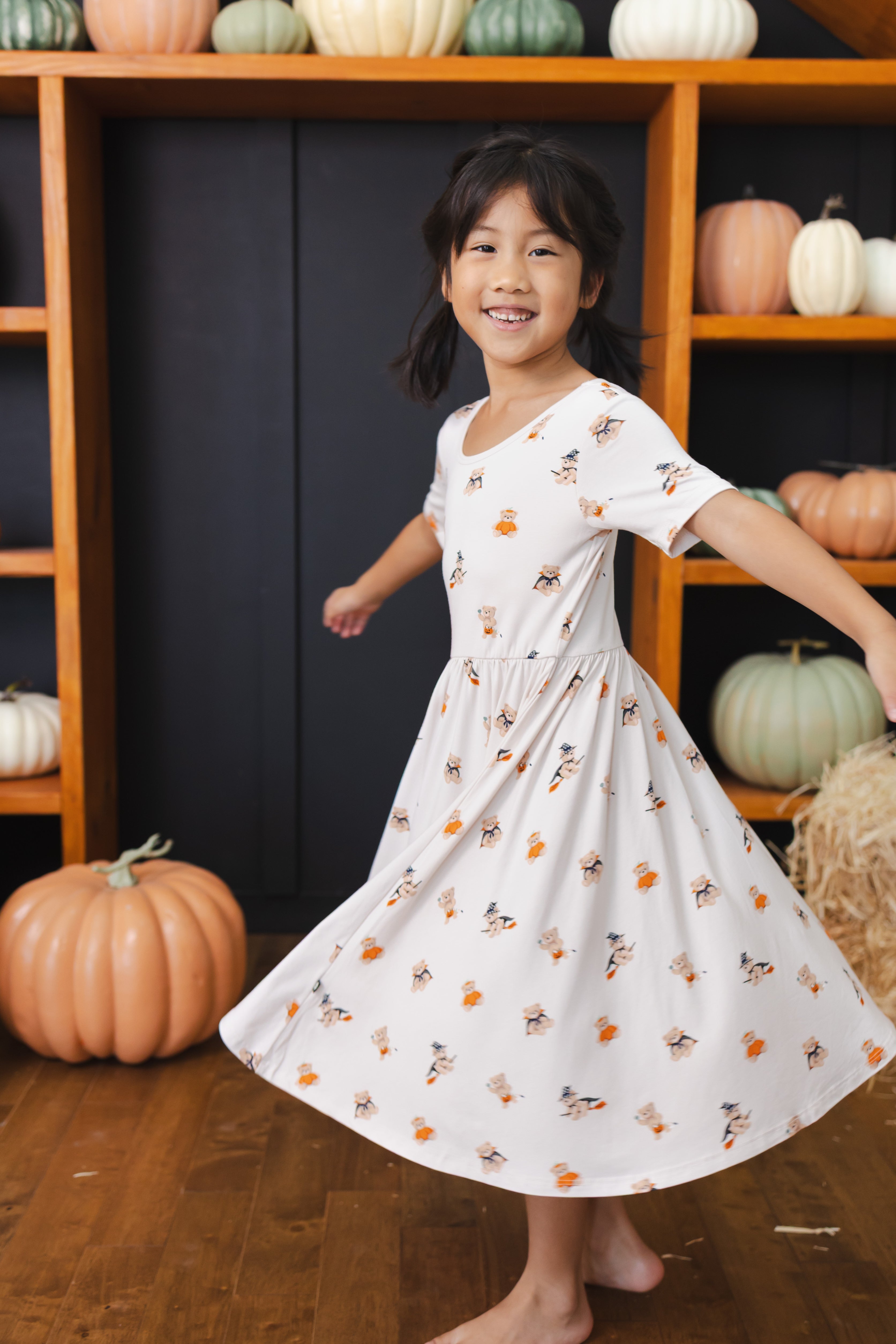 Girl twirling in Twirl Dress with Halloween Teddy print with pumpkin decorations around