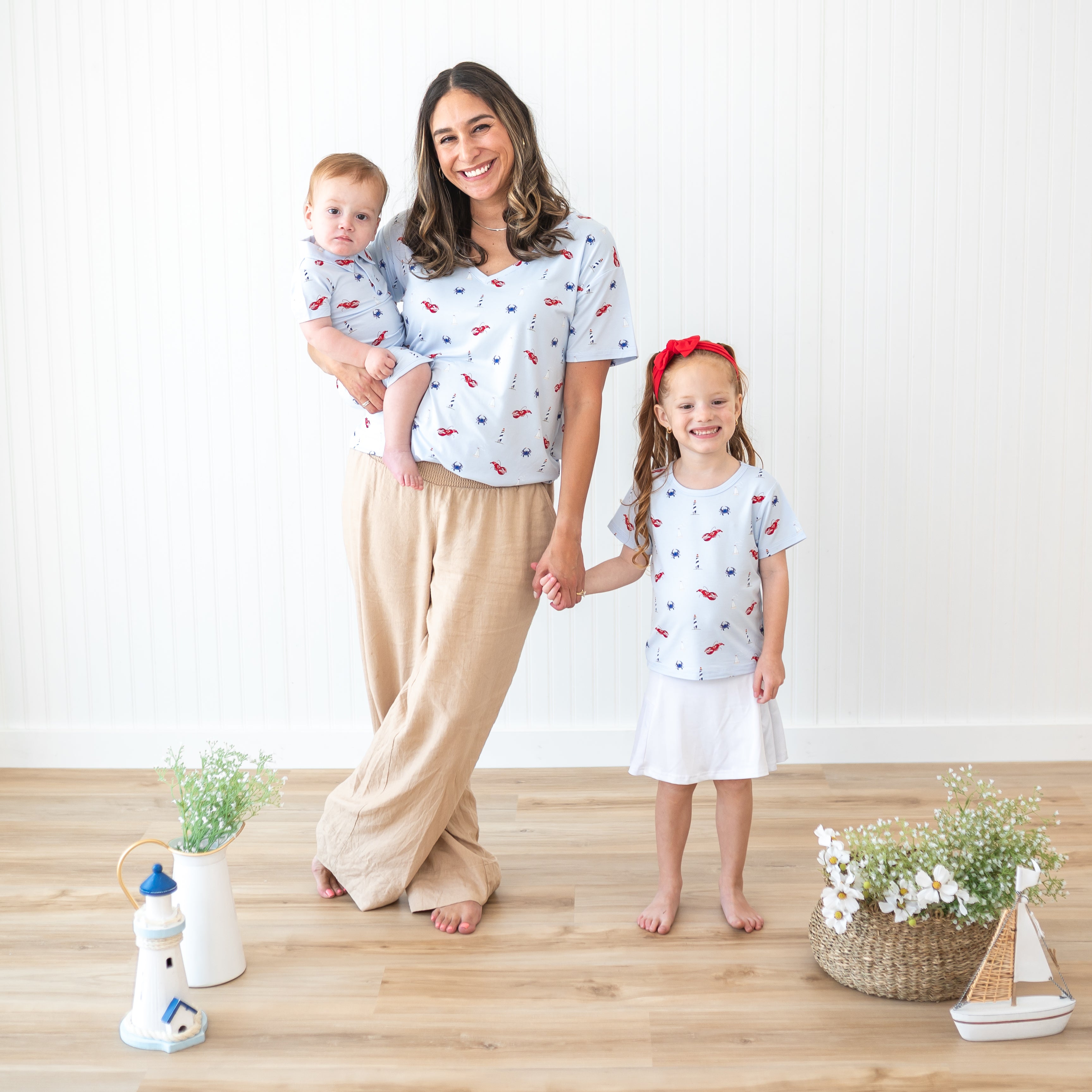 A mother standing beside her daughter holding her hand while also holding her infant son all wearing items from the Harbor collection