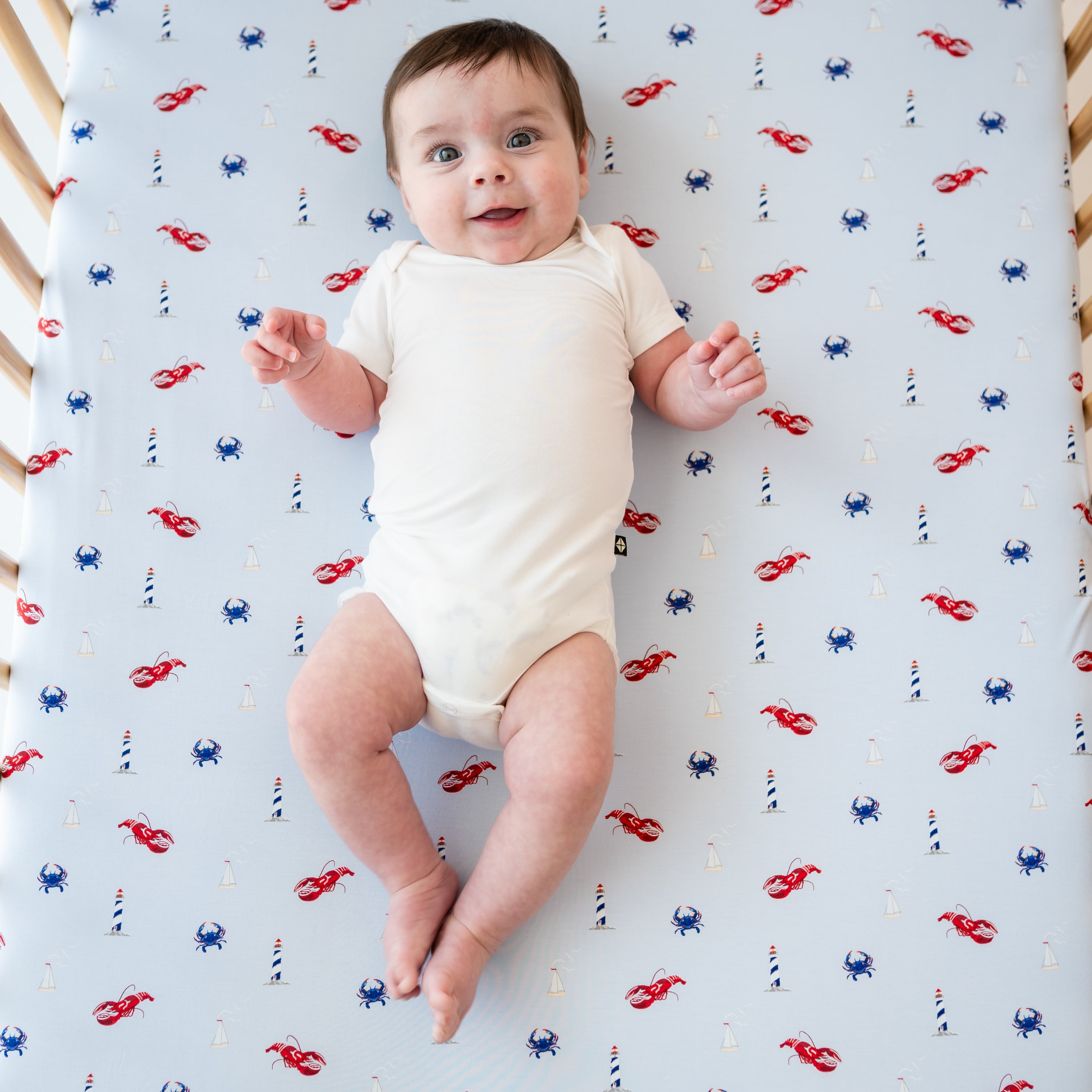 Infant laying in a crib on a Crib Sheet in Harbor wearing a Cloud Short Sleeve Bodysuit